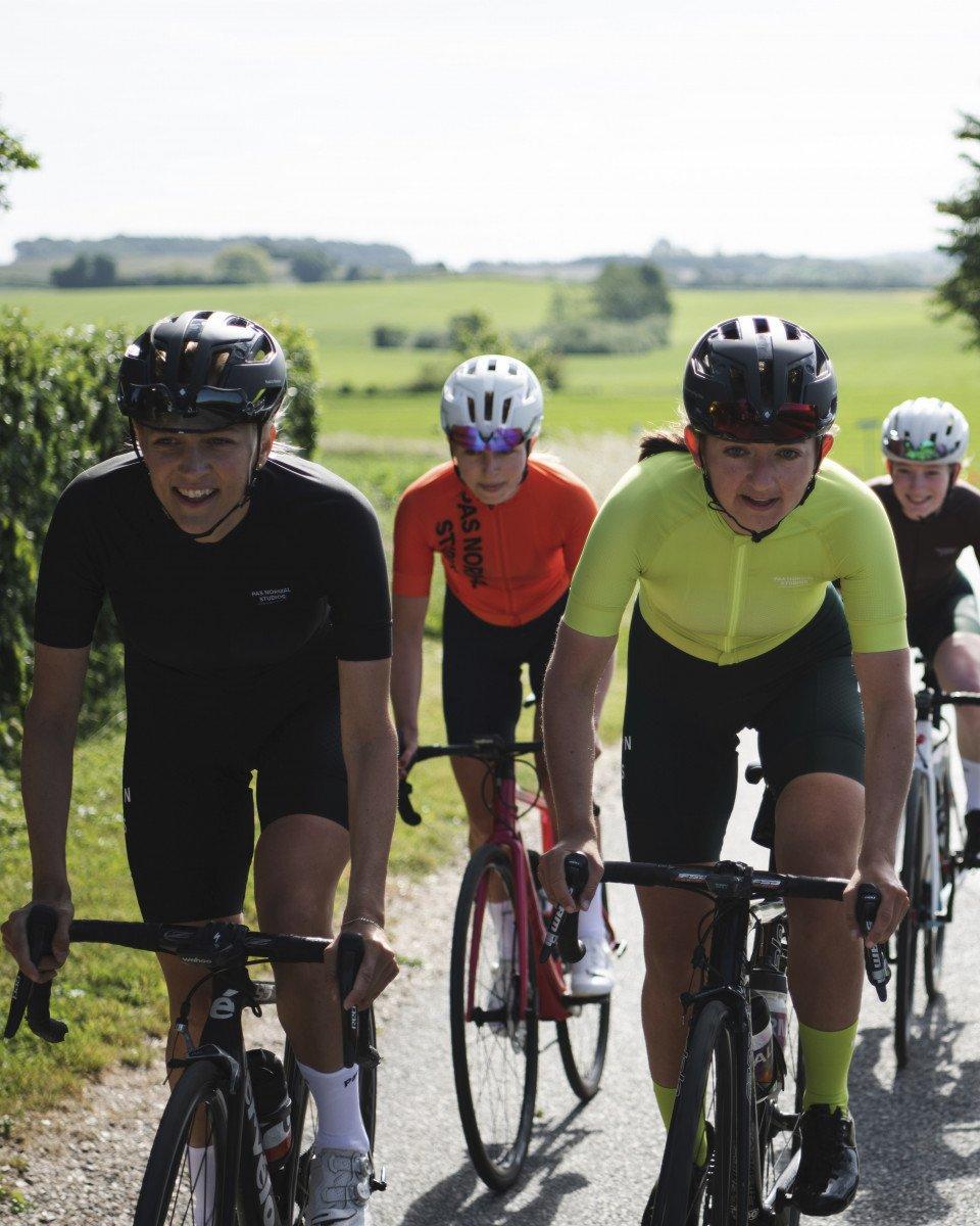 Group of cyclists in time trial position on rural road wearing aerodynamic helmets and racing attire