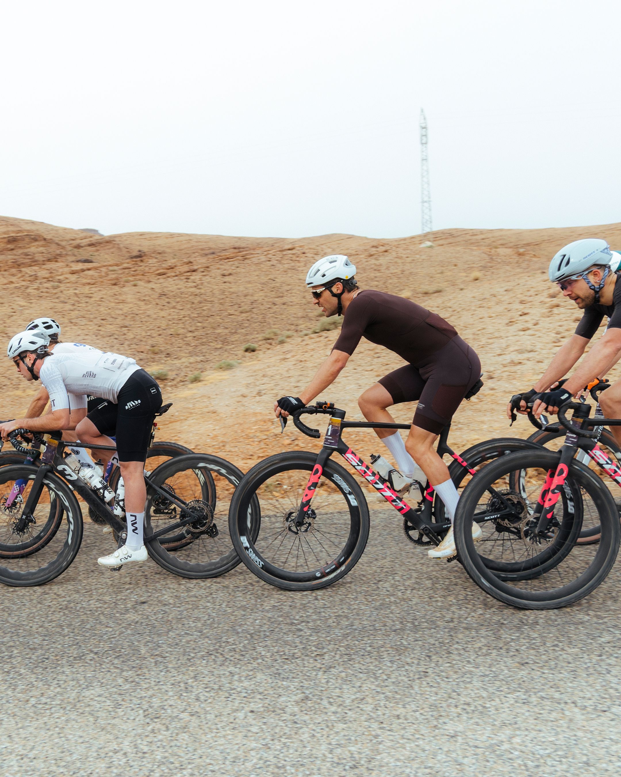Three cyclists in aero position racing on gravel road through desert landscape
