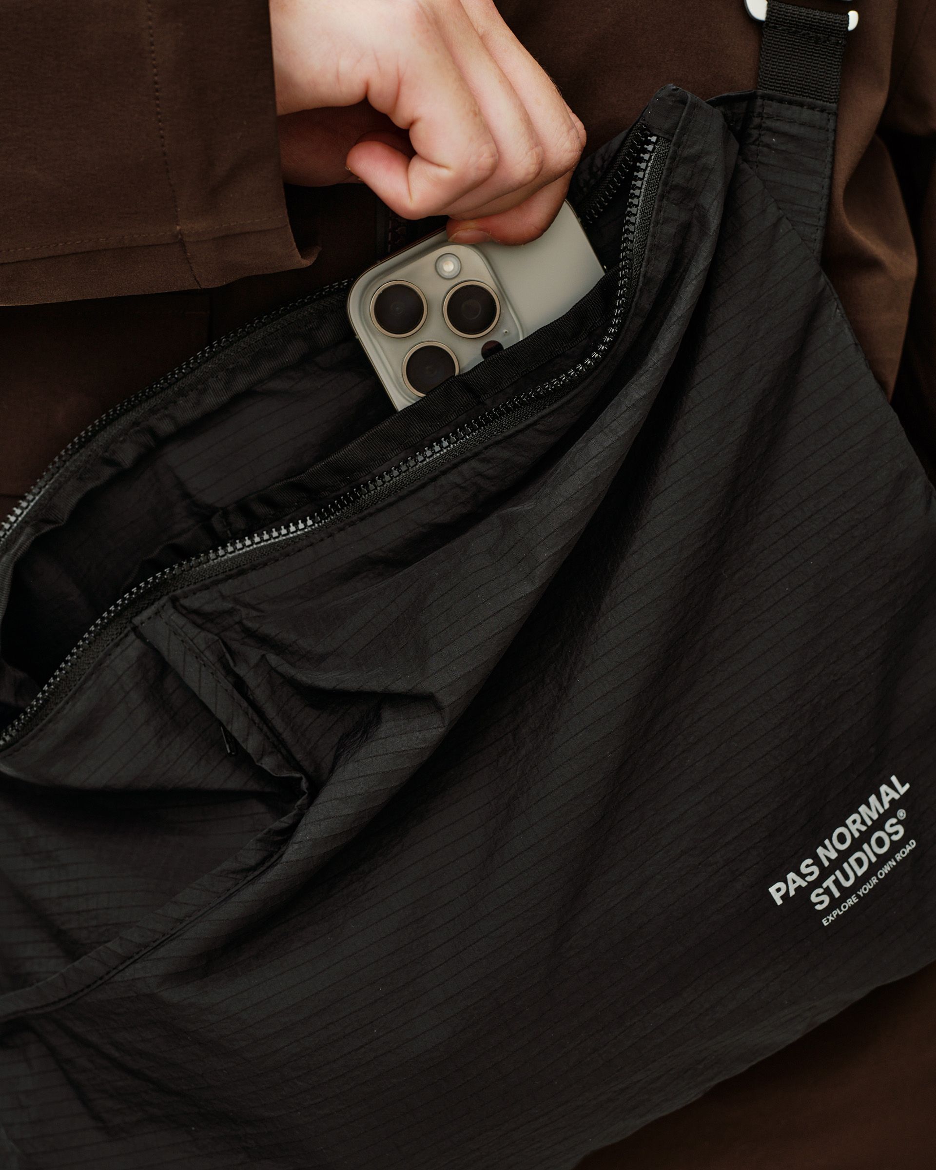 Black Off-Race Tech Musette 2.0 bag, detail view open showing interior compartment with phone being inserted