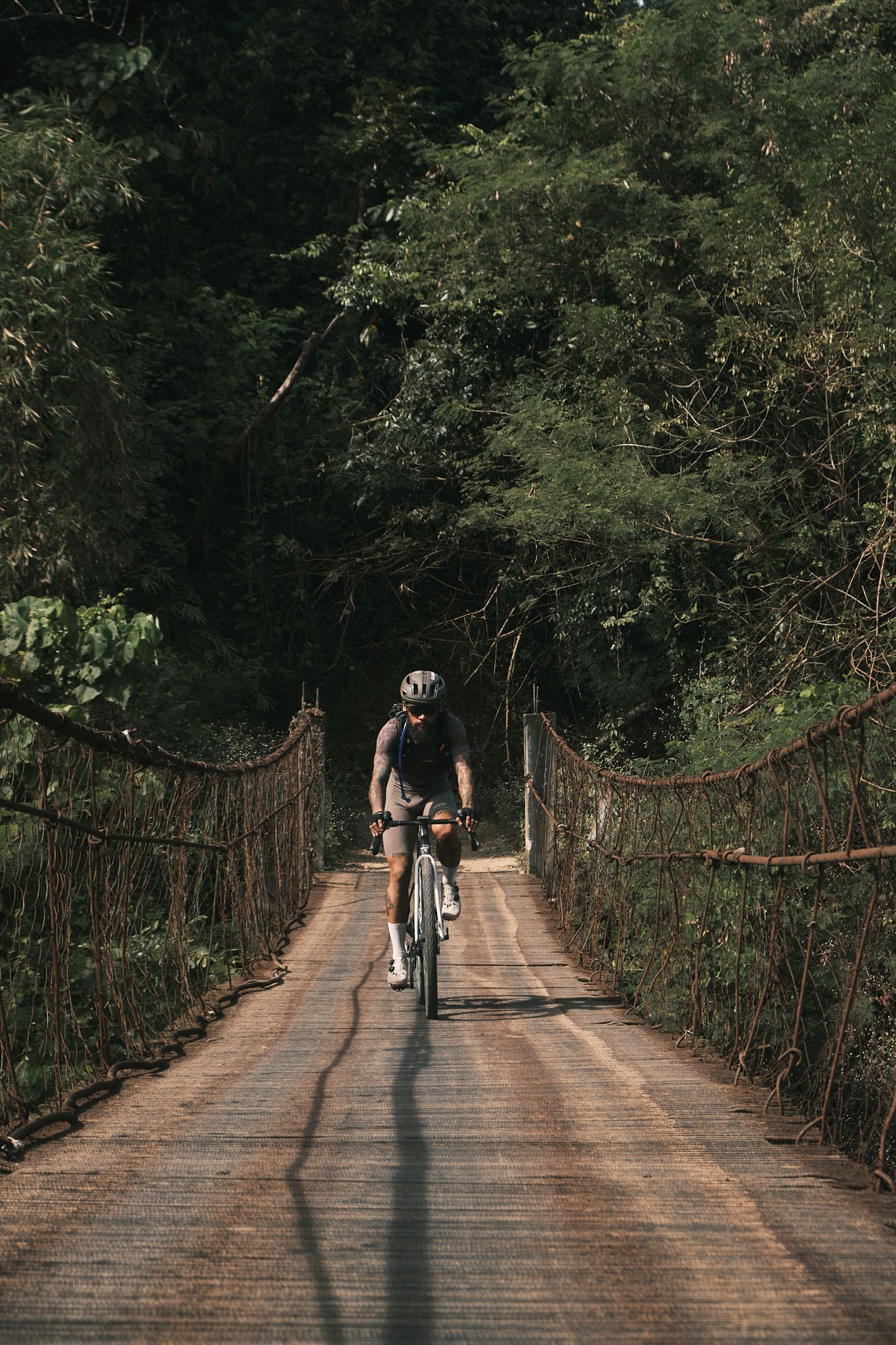 Cyclist riding across wooden bridge through forest in dark jersey and shorts