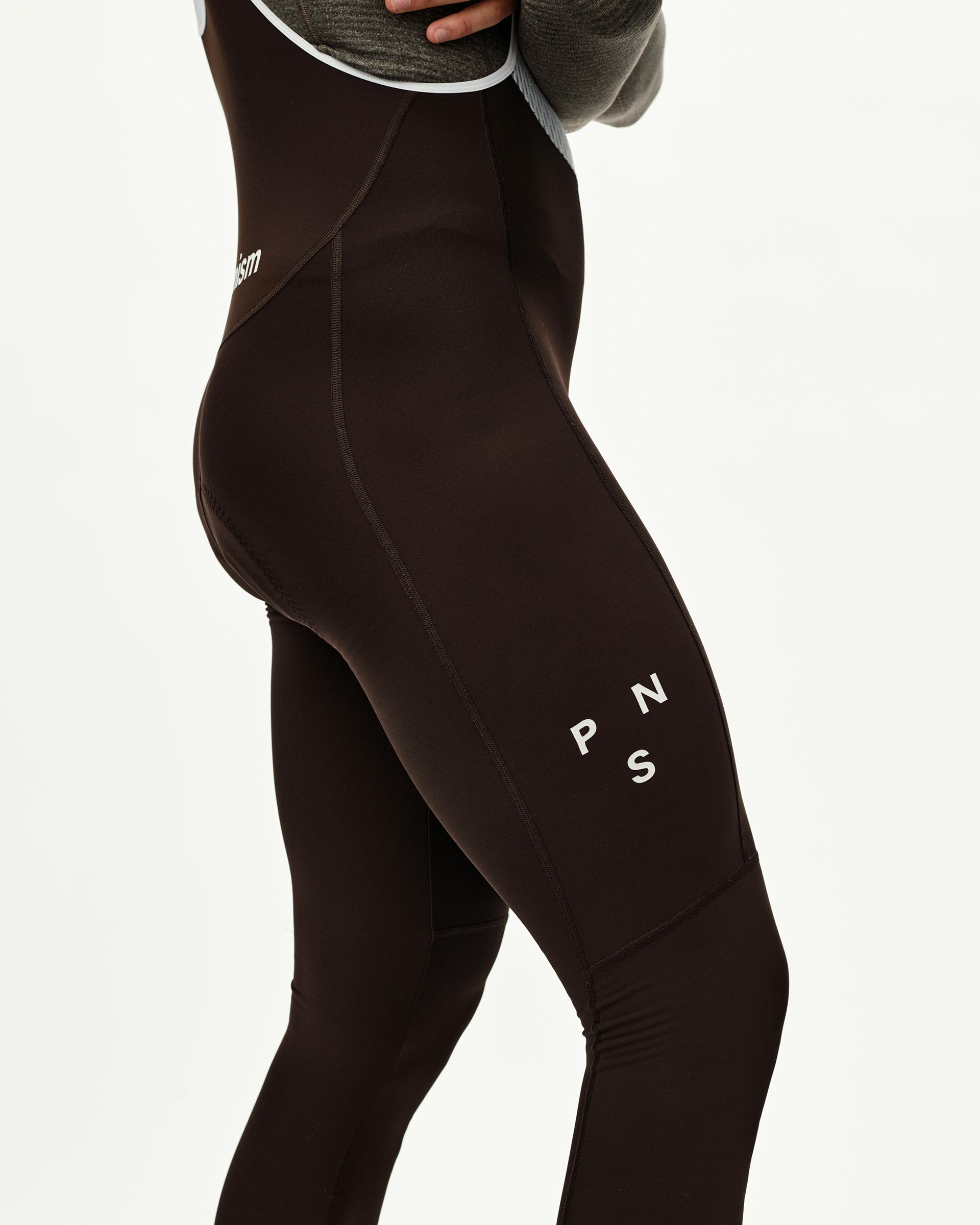 Dark Coffee brown Mechanism Thermal Long cycling bibs on model, three-quarter rear view with white logo print on thigh