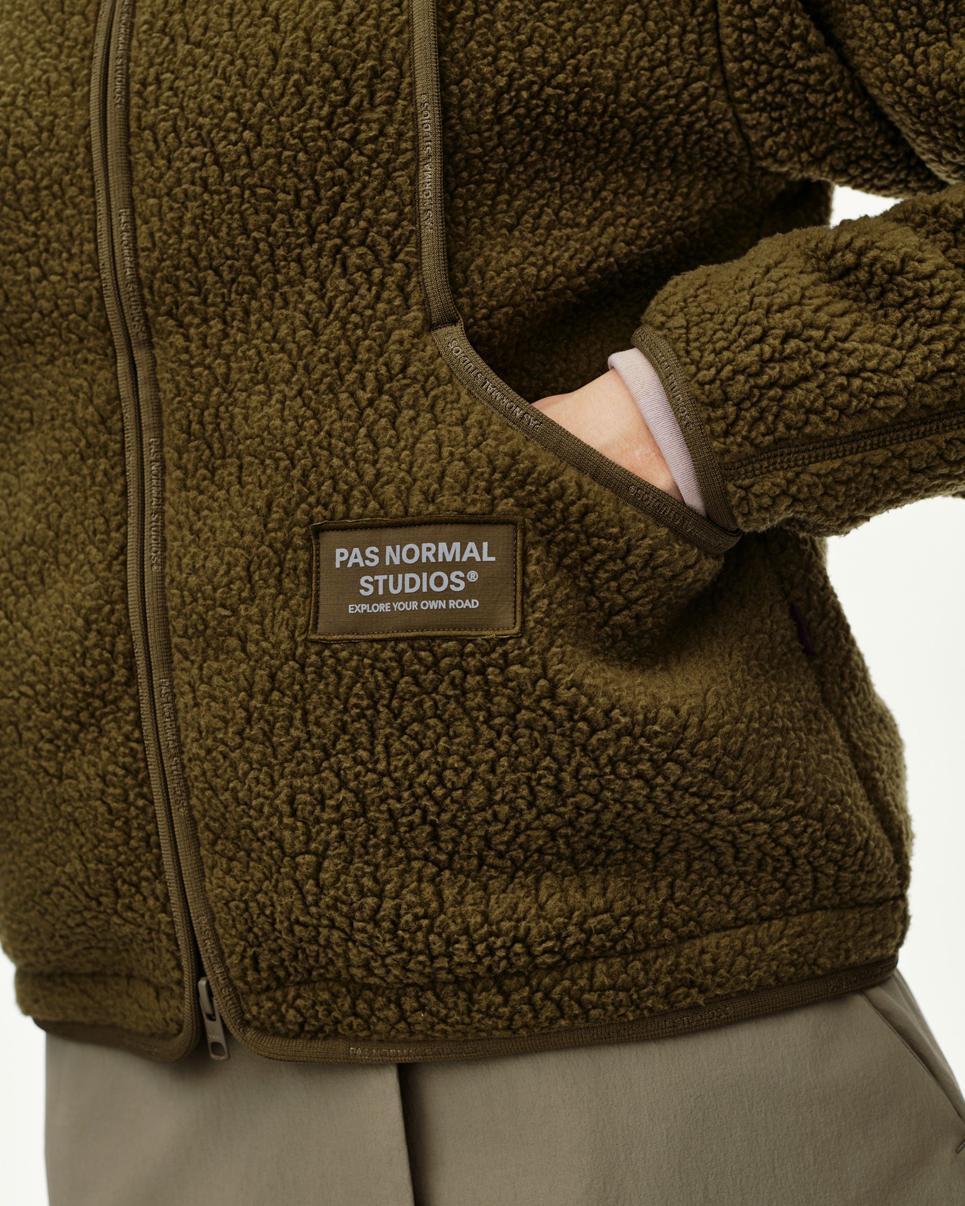 Deep Olive Off-Race Pile Fleece jacket, detail view on model showing zip pocket and woven label patch