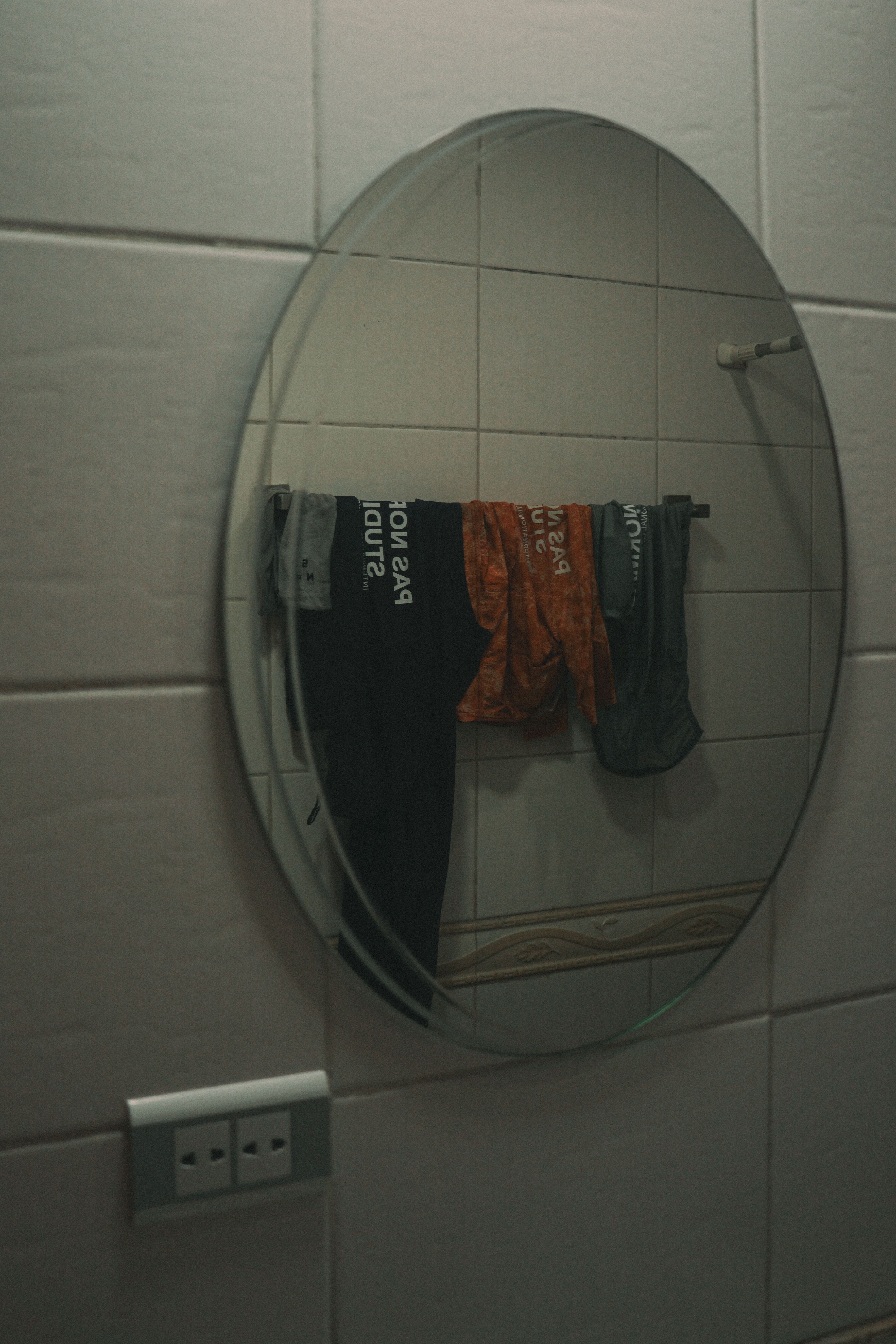 Cycling apparel reflected in round bathroom mirror, showing black and orange garments hanging