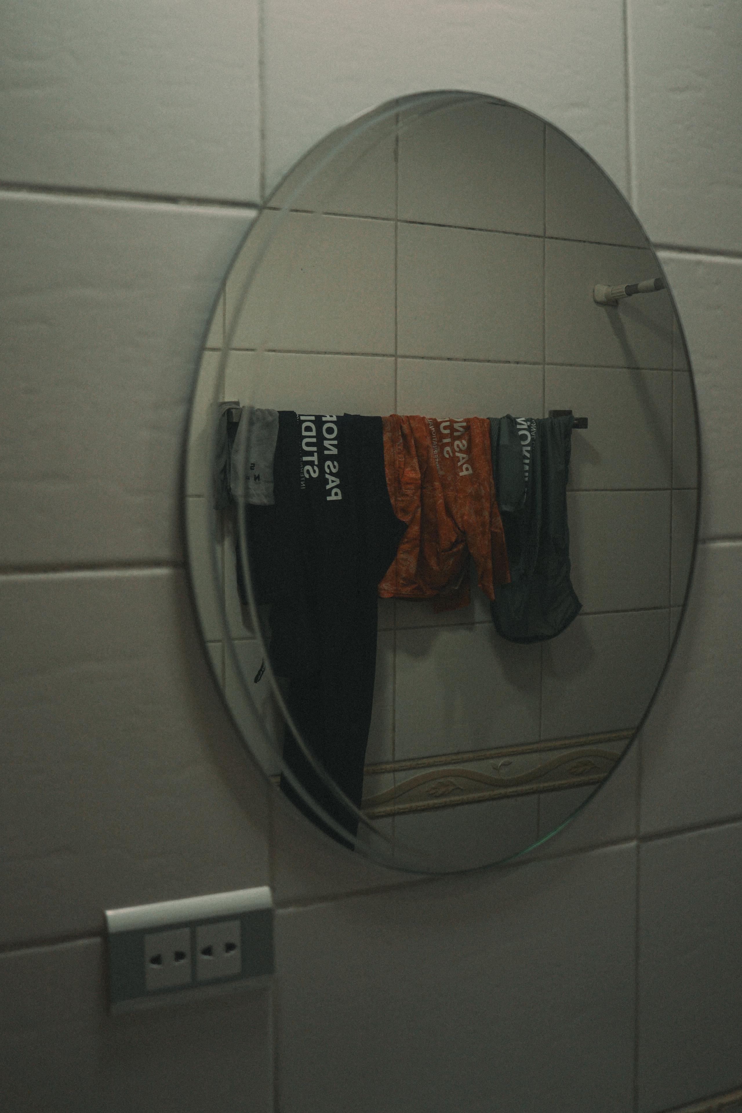 Cycling apparel reflected in round bathroom mirror, showing black and orange garments hanging