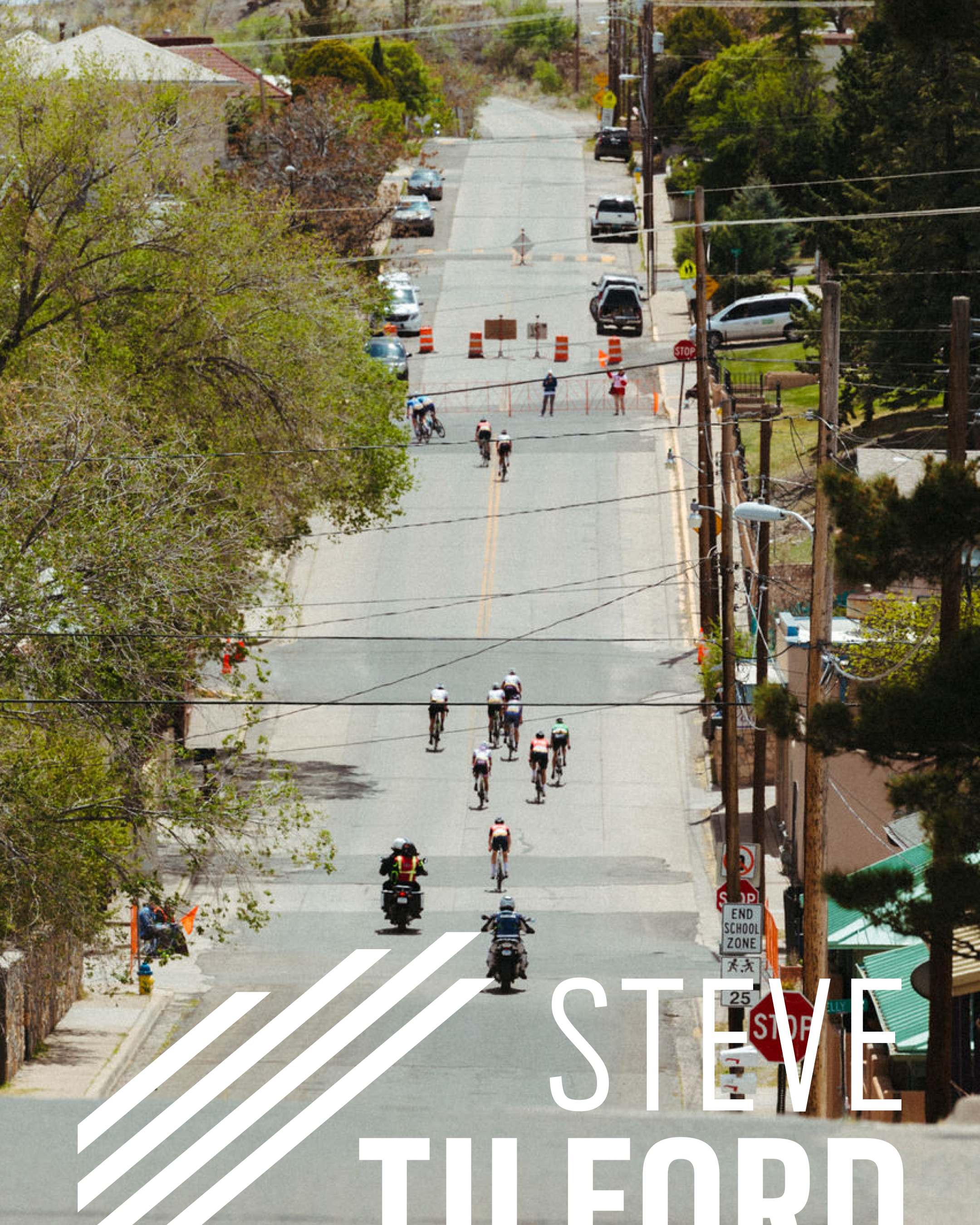 Cyclists racing uphill on steep residential street during Tour of the Gila with support vehicles following