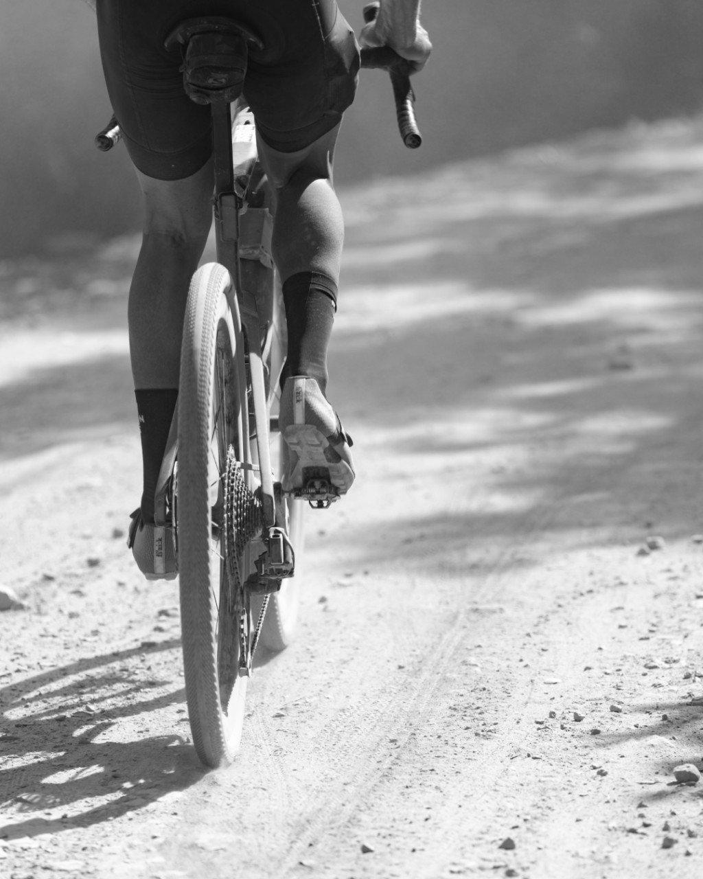 Cyclist riding on gravel road wearing dark shorts and socks, black and white photography