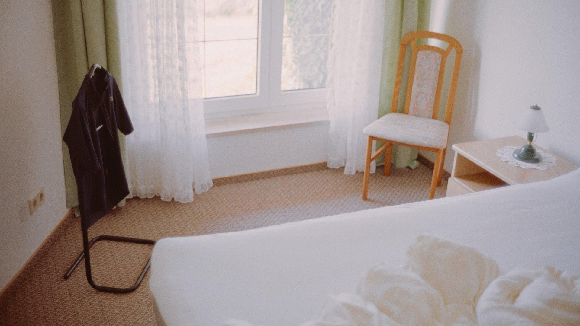 Dark cycling jacket hanging on chair in bright hotel room with unmade bed