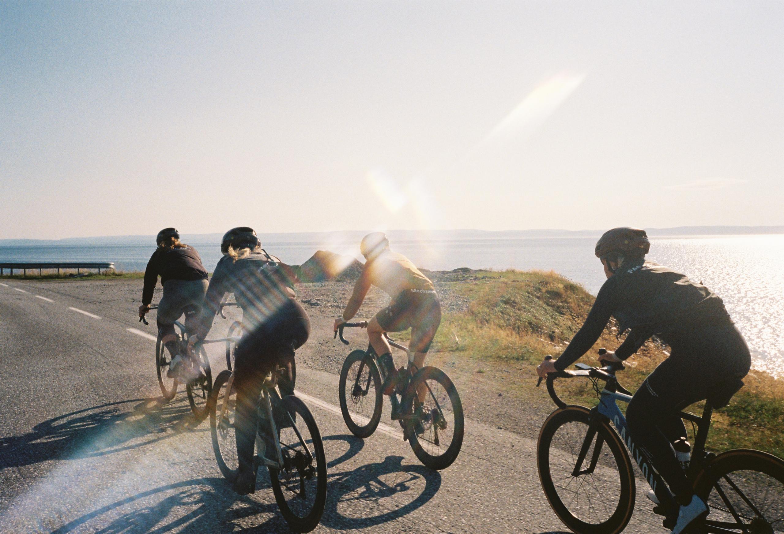 Four cyclists riding on coastal road at sunset with ocean backdrop