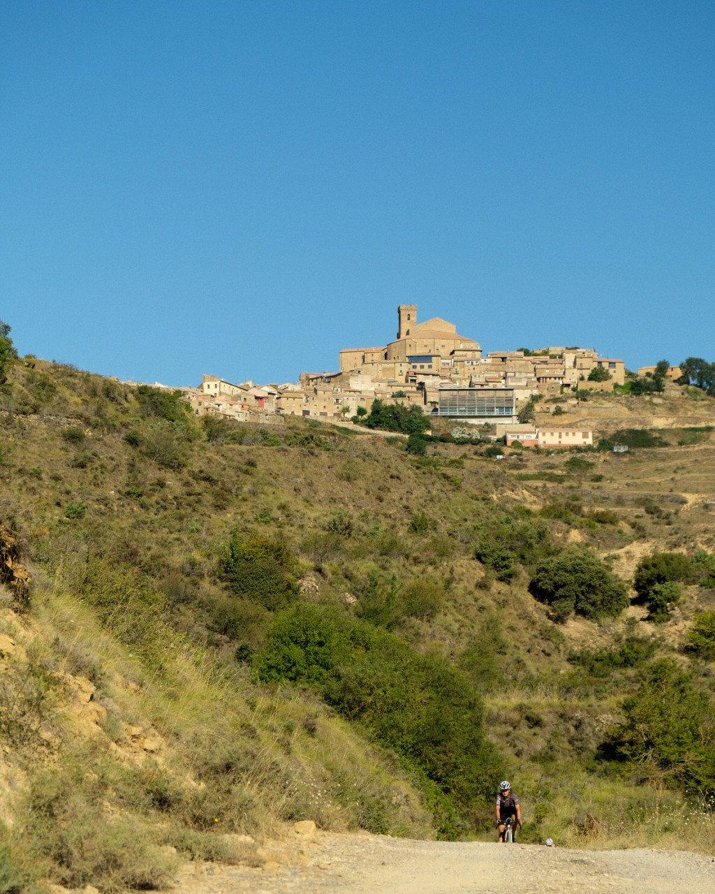 Cyclist on gravel road through Mediterranean hillside with hilltop village above