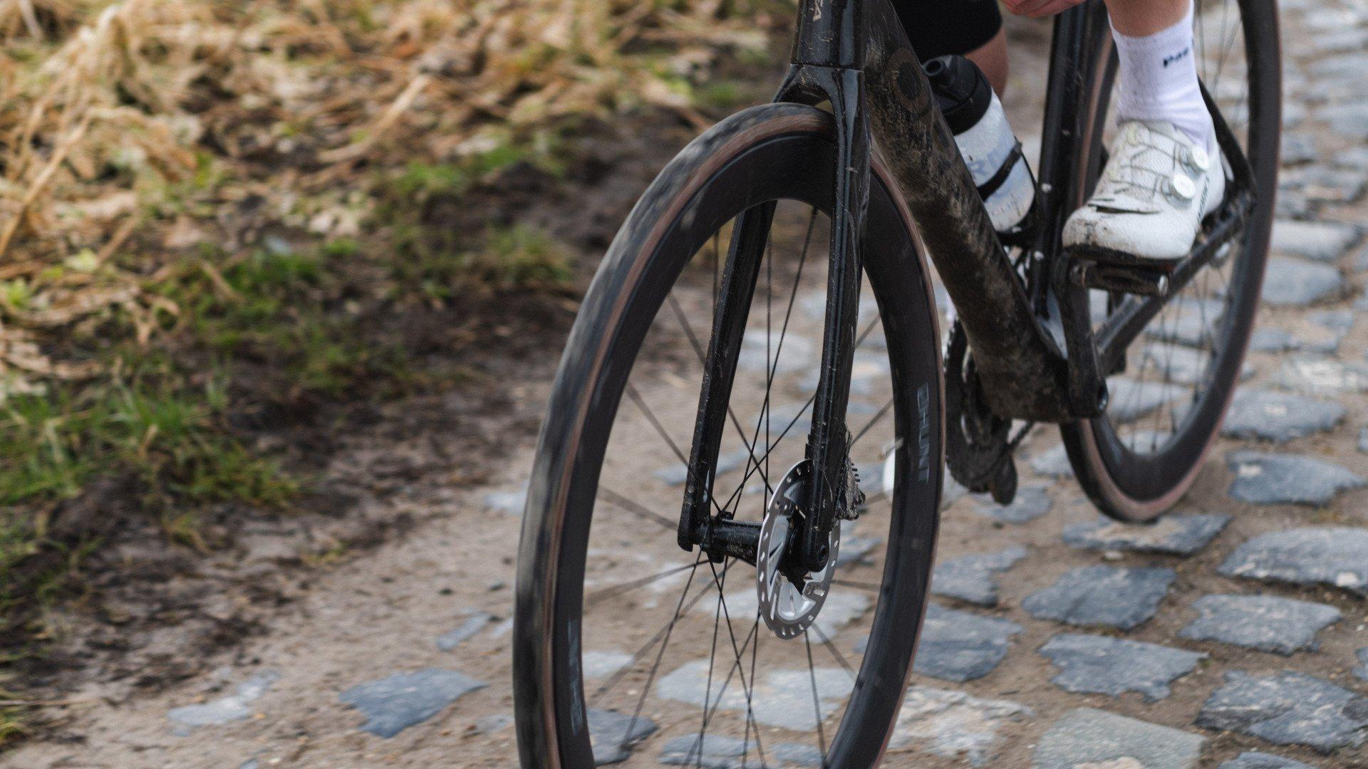 Close-up of bicycle wheel and disc brake on cobblestone surface with cyclist in white clothing