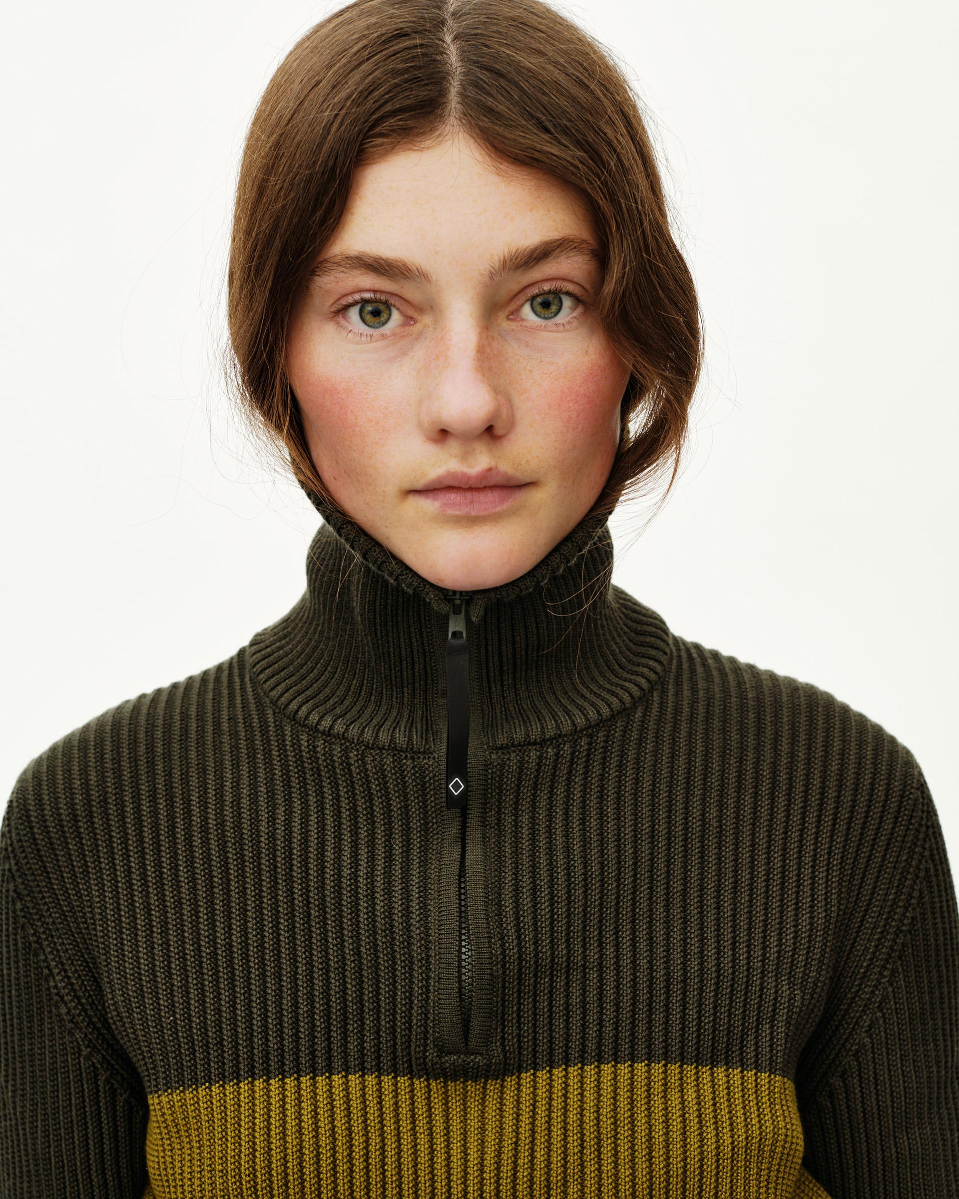 Olive Off-Race Merino Knit Half-Zip sweater on model, front close-up with contrast yellow stripe and ribbed turtleneck