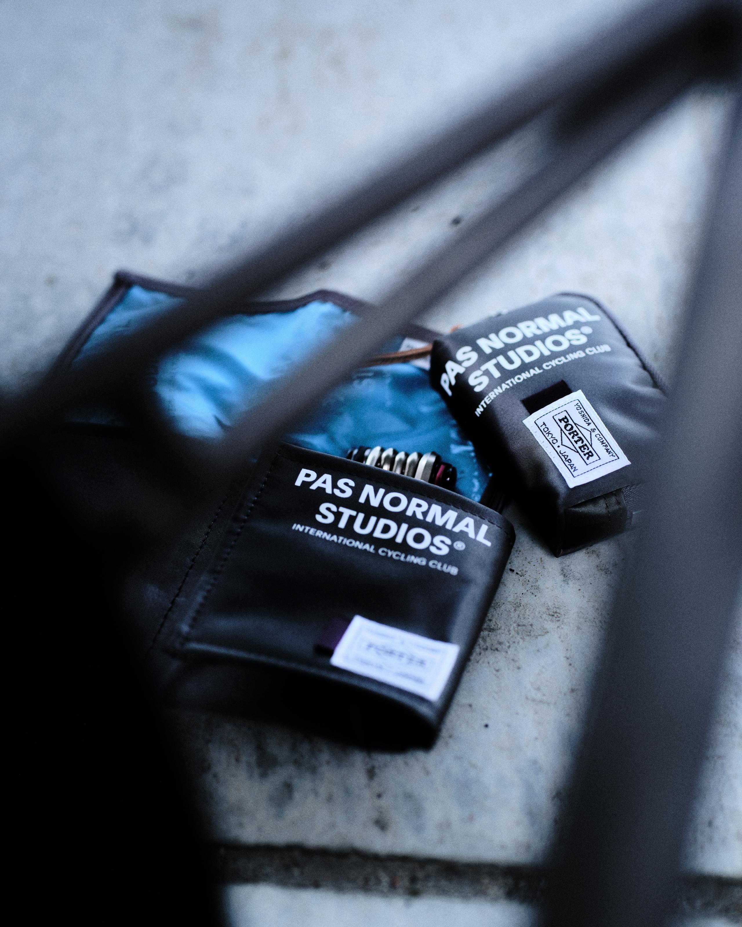 Black cycling accessories with brand logos laid on concrete surface with blue cycling shoes in background