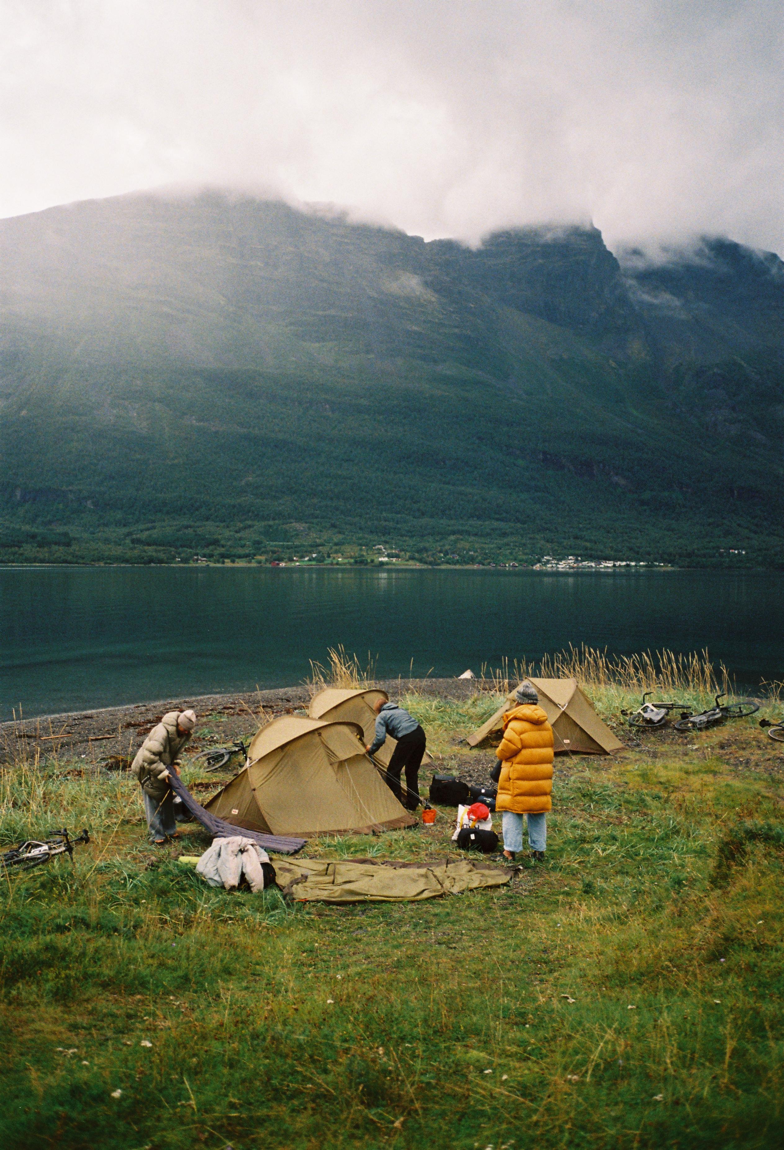 Camping scene with tents by lake and misty mountains in background