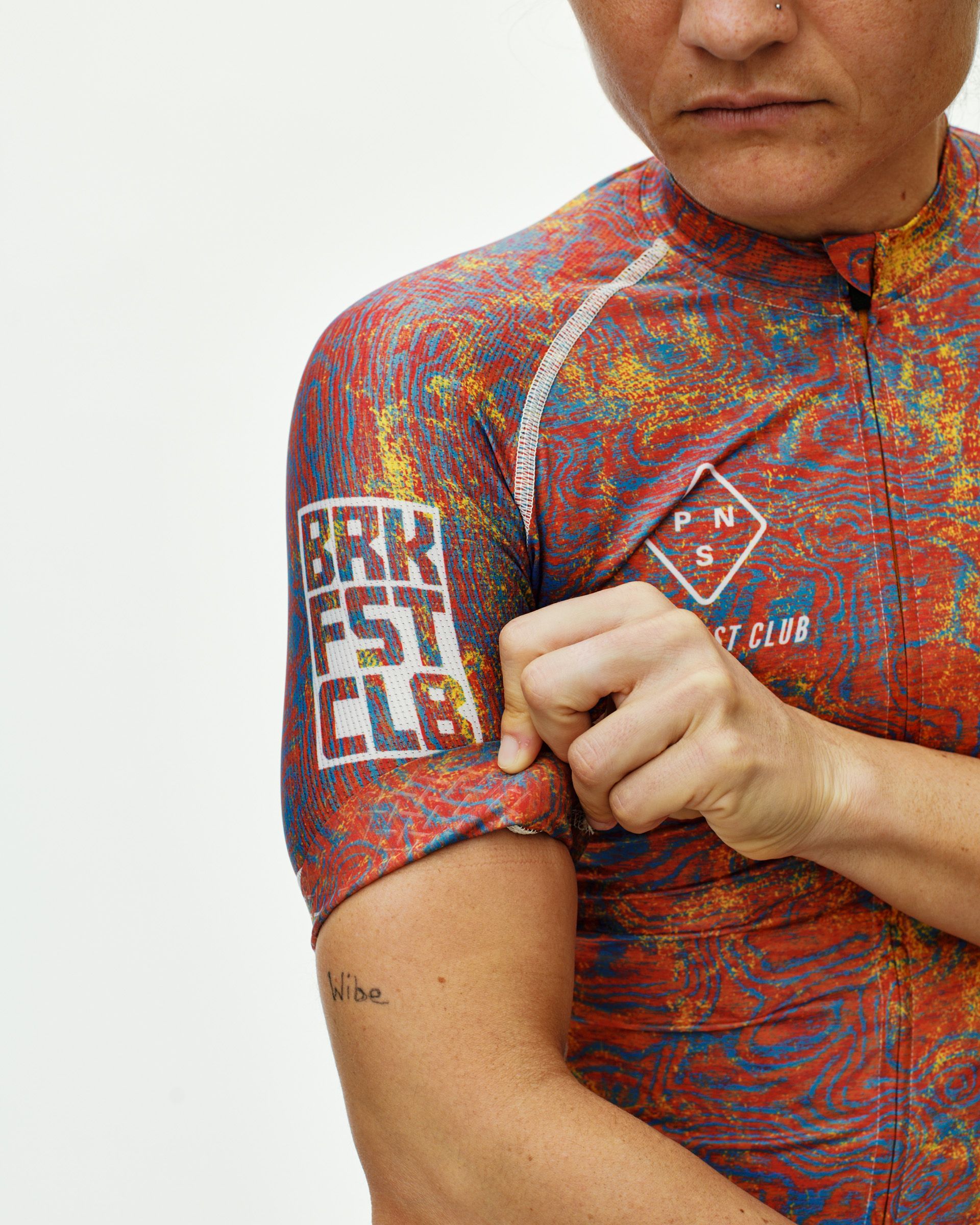 Breakfast Club red multicolor Mechanism cycling jersey on model, front detail with swirl AOP and sleeve logo print