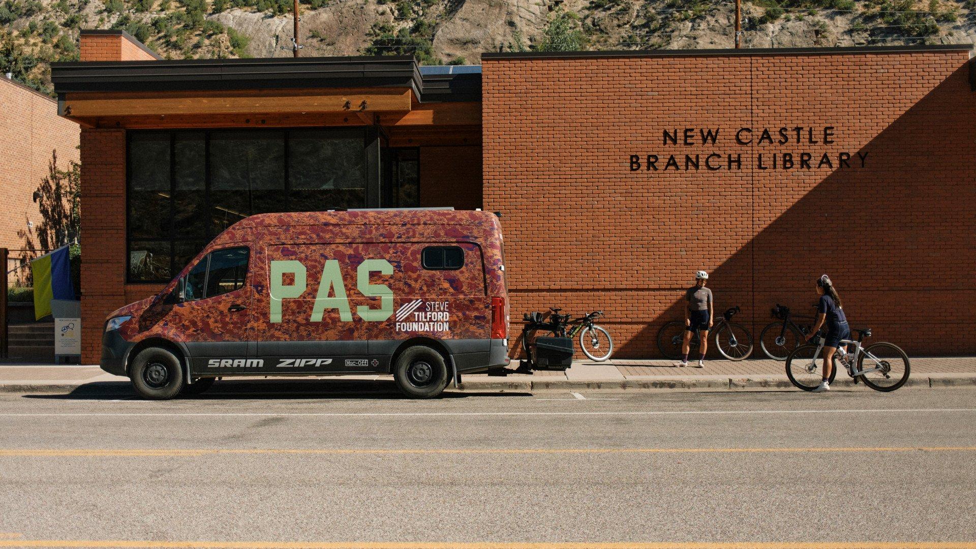 PAS collection support van parked outside New Castle Branch Library with cyclists preparing bikes