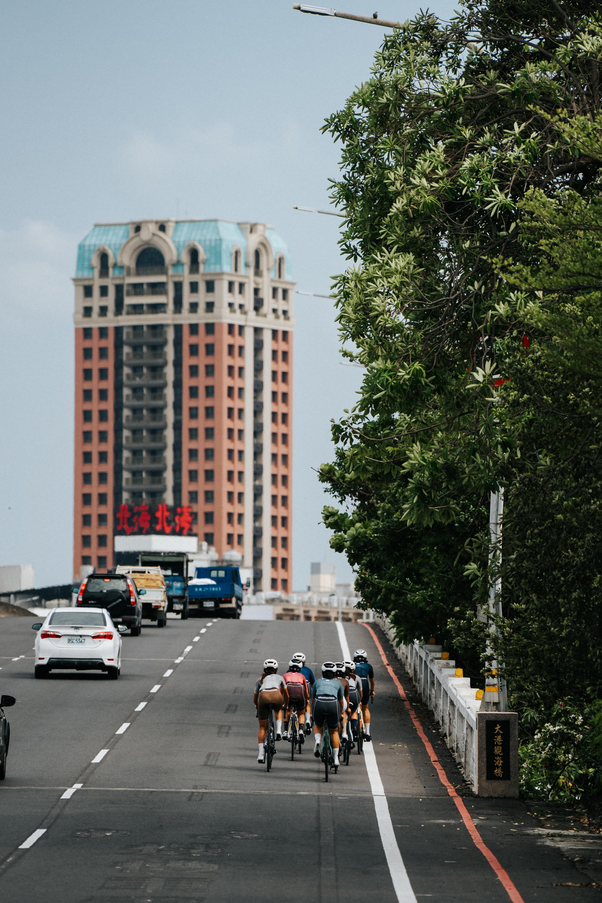 Cyclists riding in formation on urban road with tall building and traffic in background