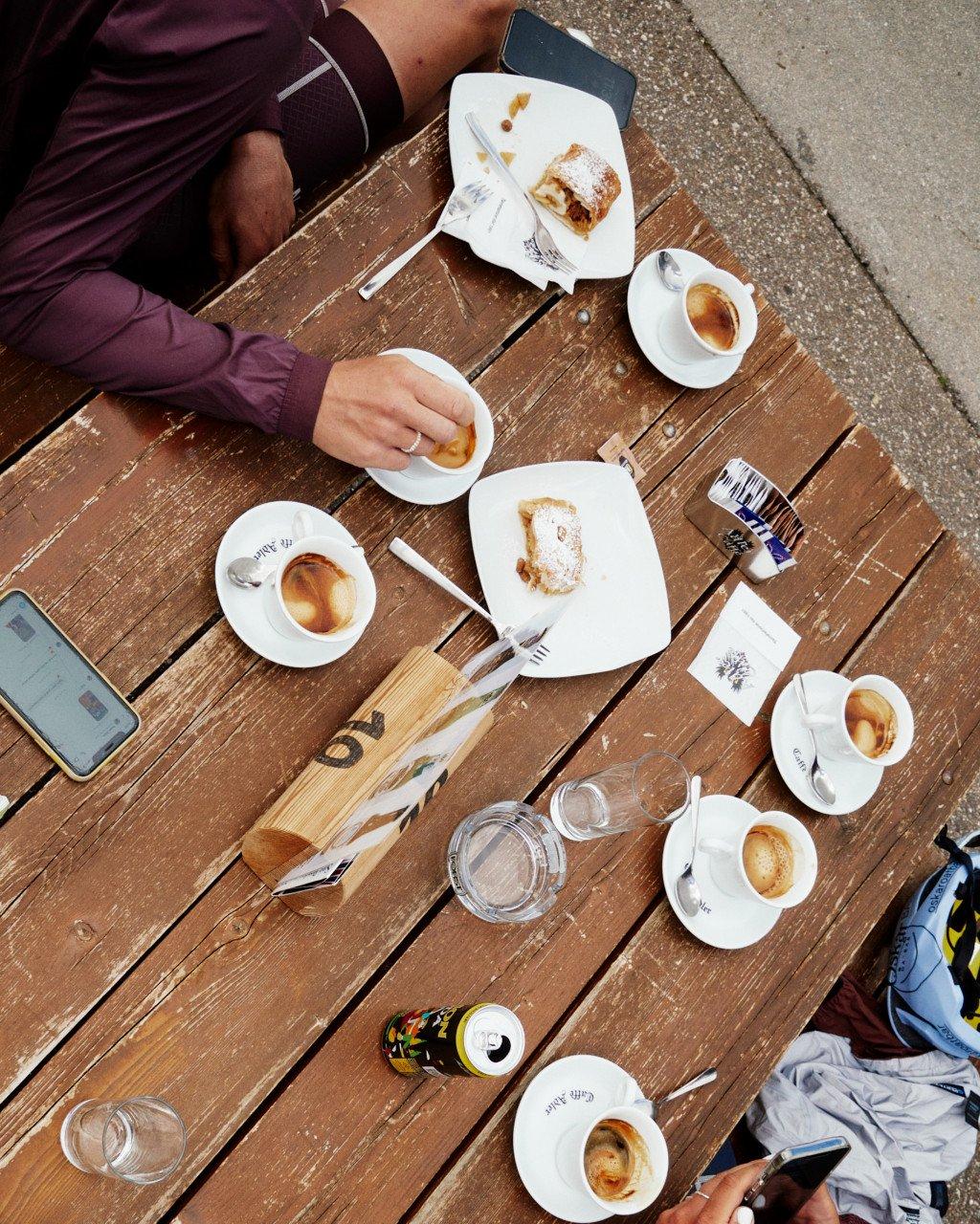 Cyclist in burgundy jersey at outdoor cafe table with coffee and pastries