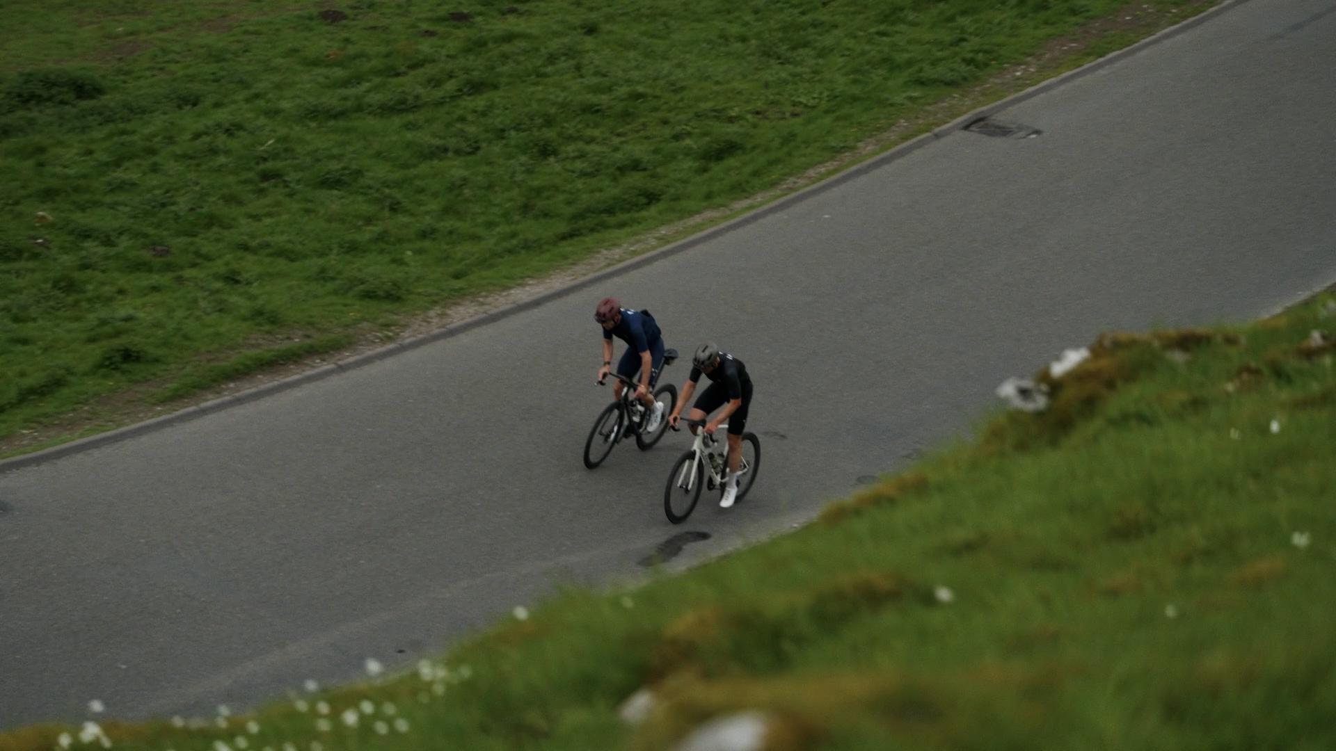 Two cyclists in dark jerseys racing on road through green countryside landscape