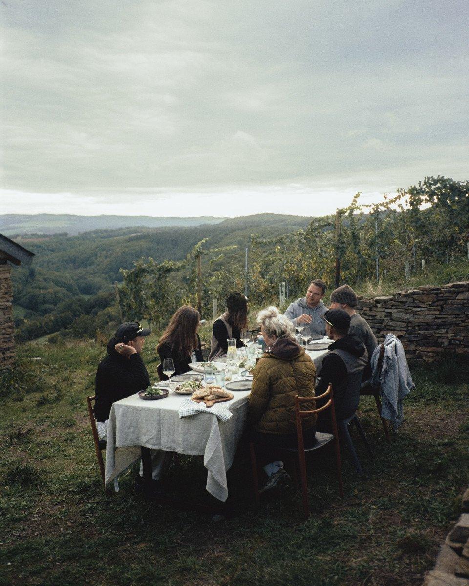 Group dining outdoors at table with rolling hills landscape in background