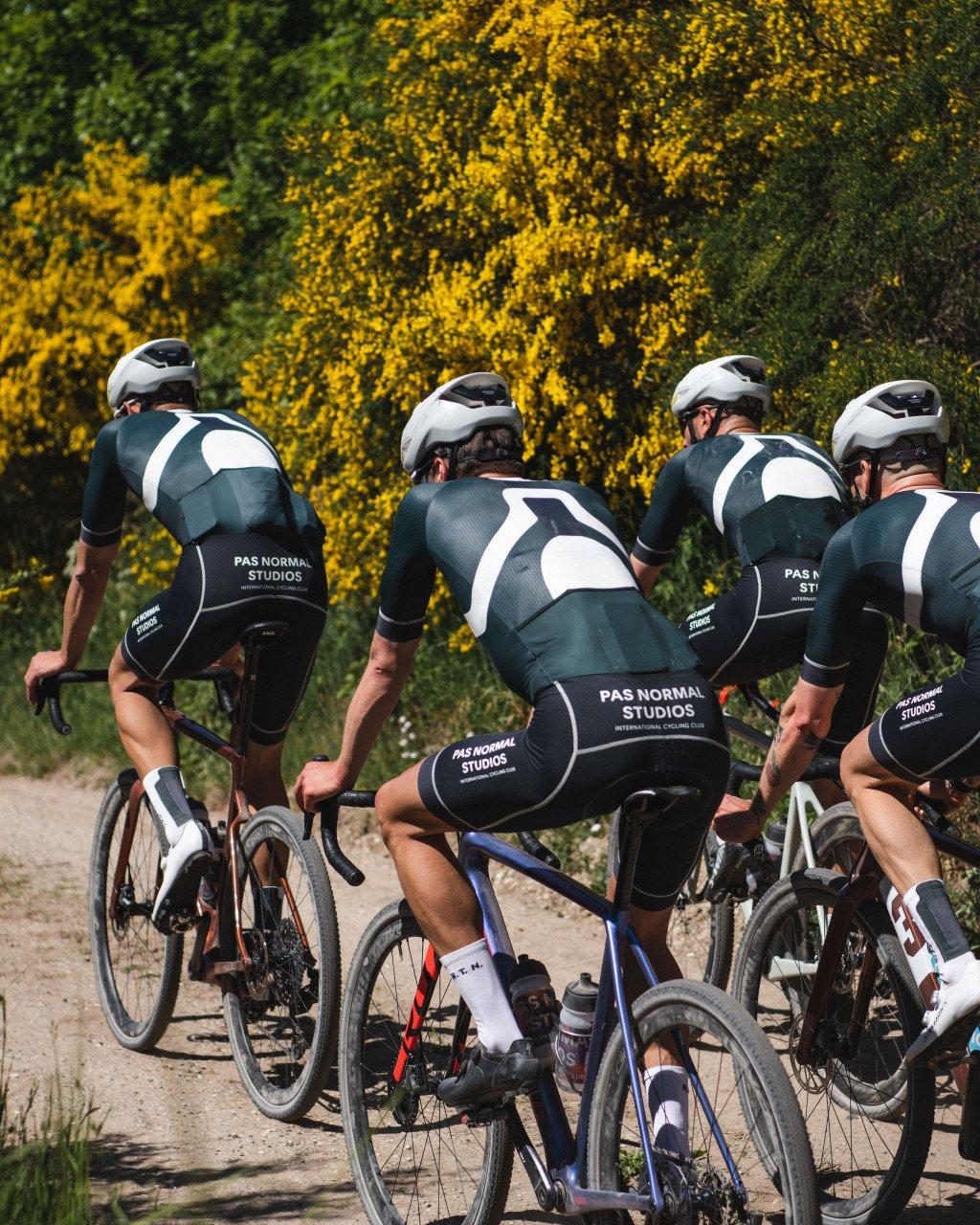 Cycling team in aerodynamic position wearing dark green and white time trial suits with matching helmets on road