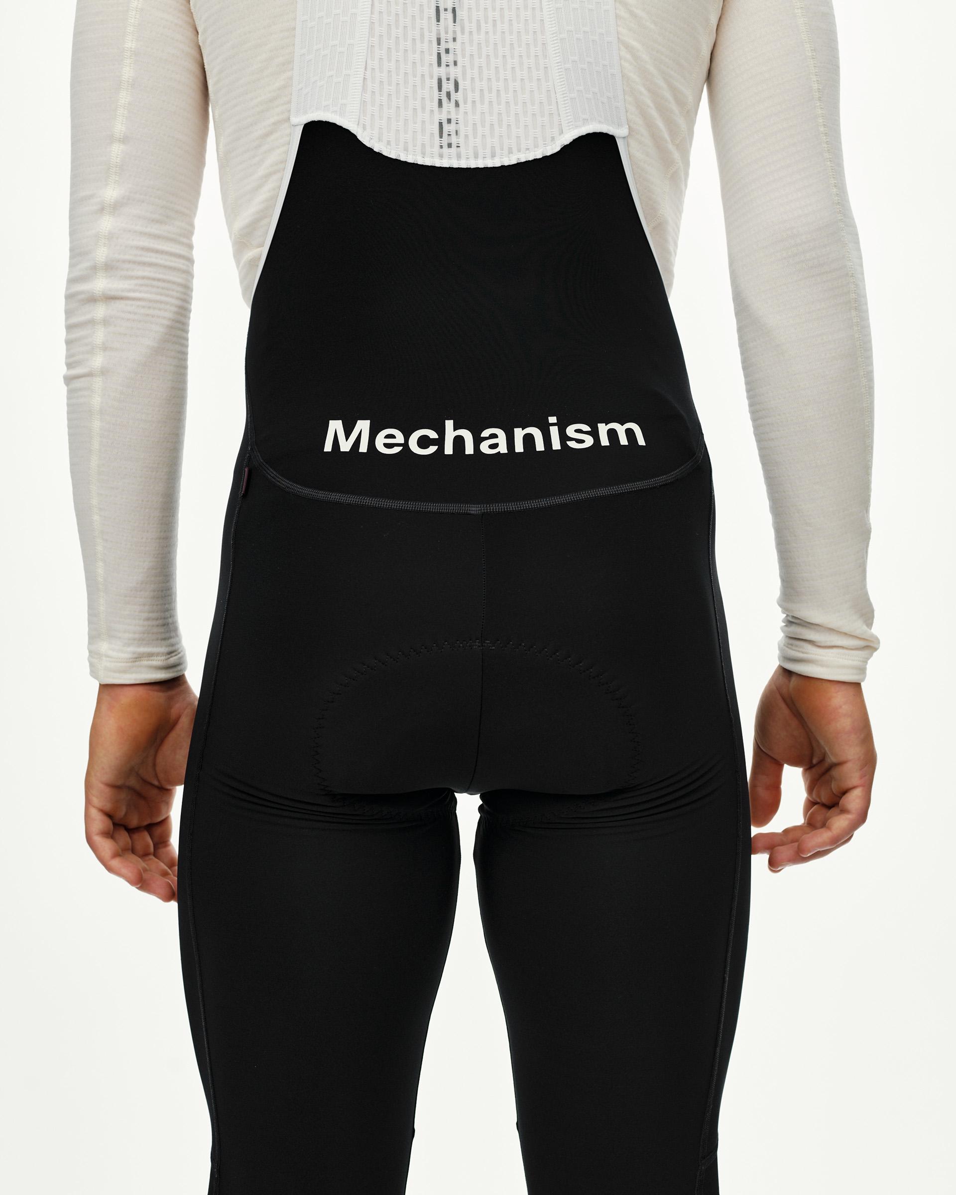 Black Mechanism cycling thermal long bibs on model, rear view with white wordmark and back pocket
