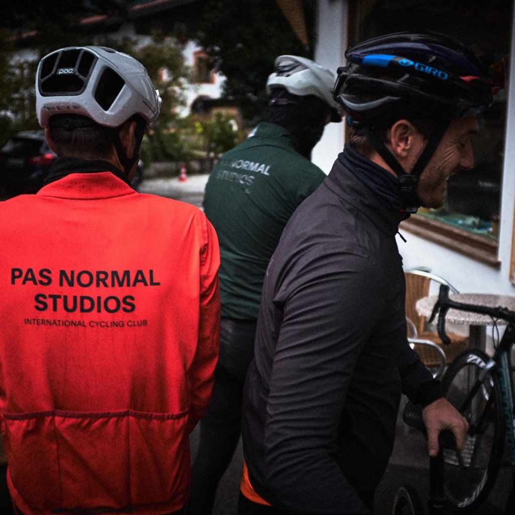 Cyclists at coffee stop wearing red cycling jacket with back branding and green jersey