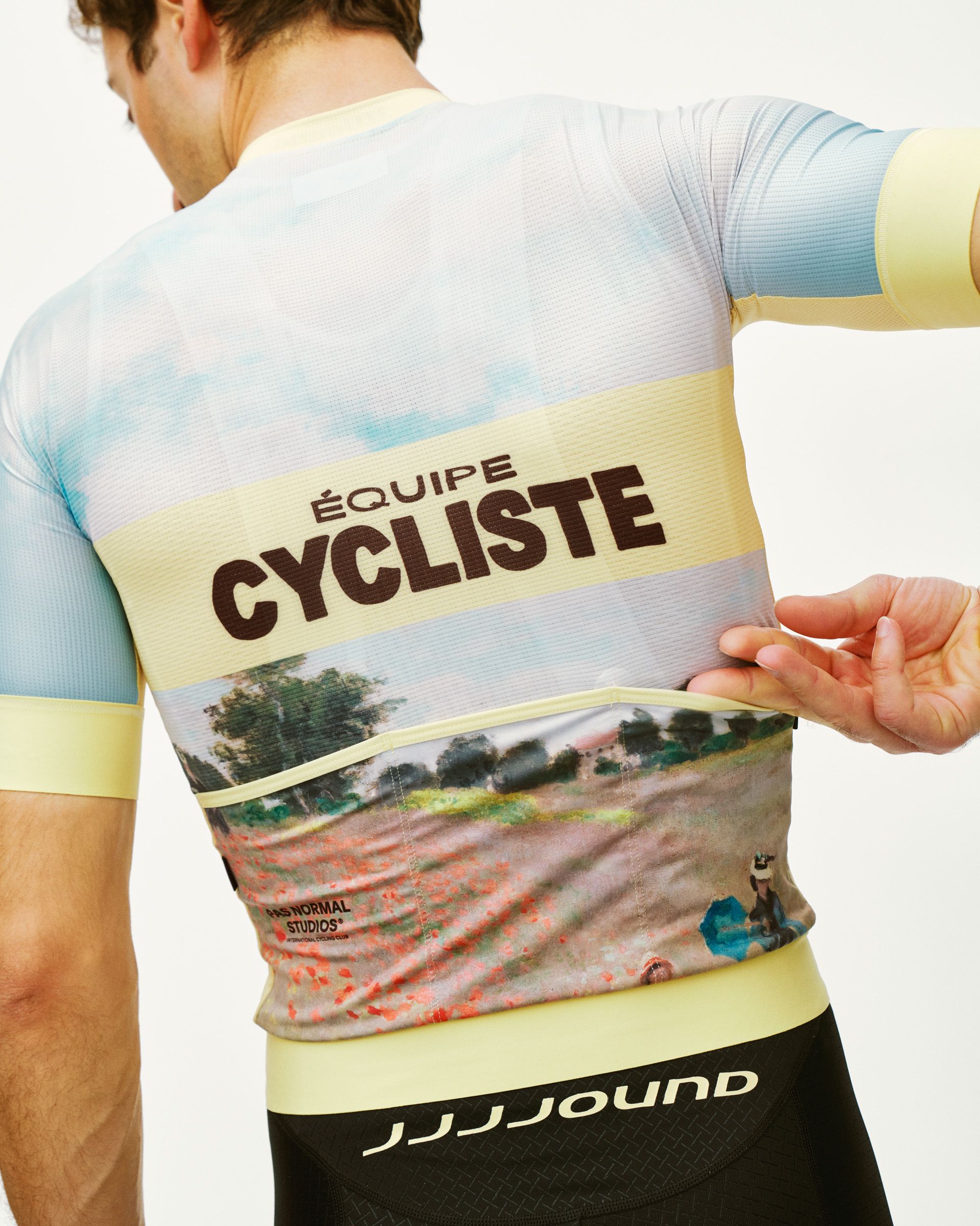 Model wearing JJJJound collaboration jersey with yellow trim, cycling graphics and landscape photography print on back