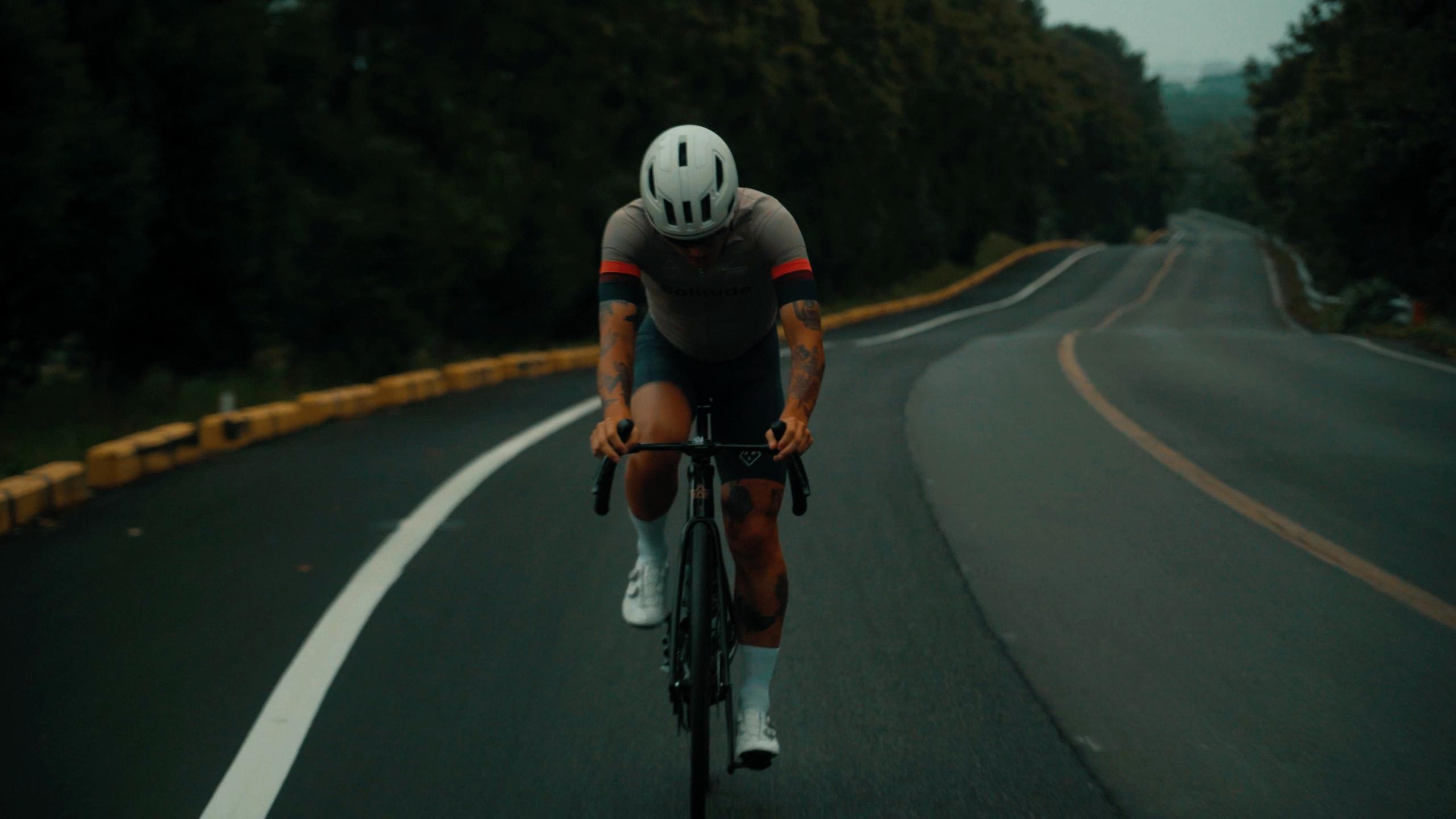 Model wearing dark cycling skinsuit with red sleeve accents, aerodynamic position on road
