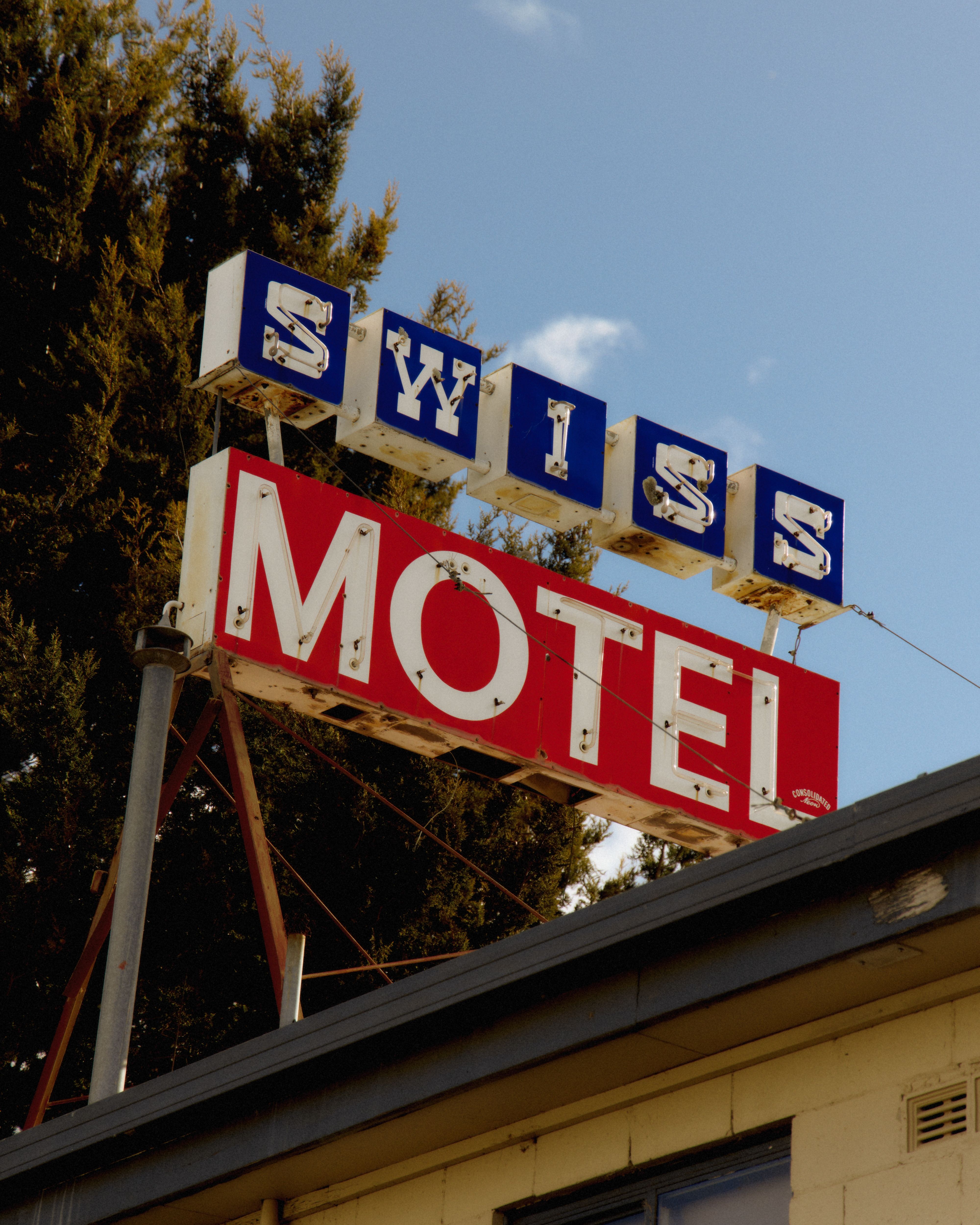 Vintage motel sign with red and blue lettering against blue sky and trees