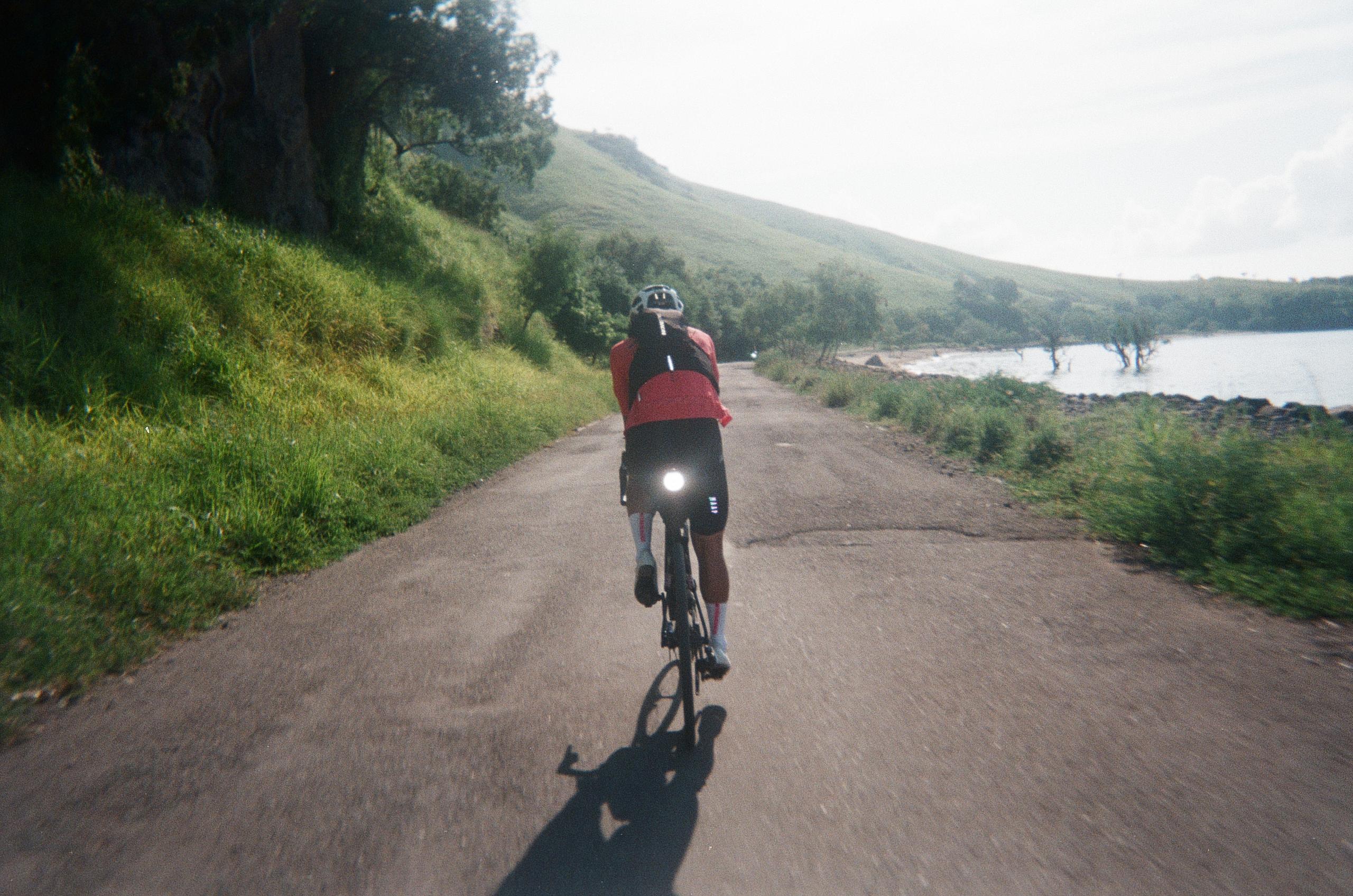 Cyclist in red jersey riding on rural road through green hills and lake landscape