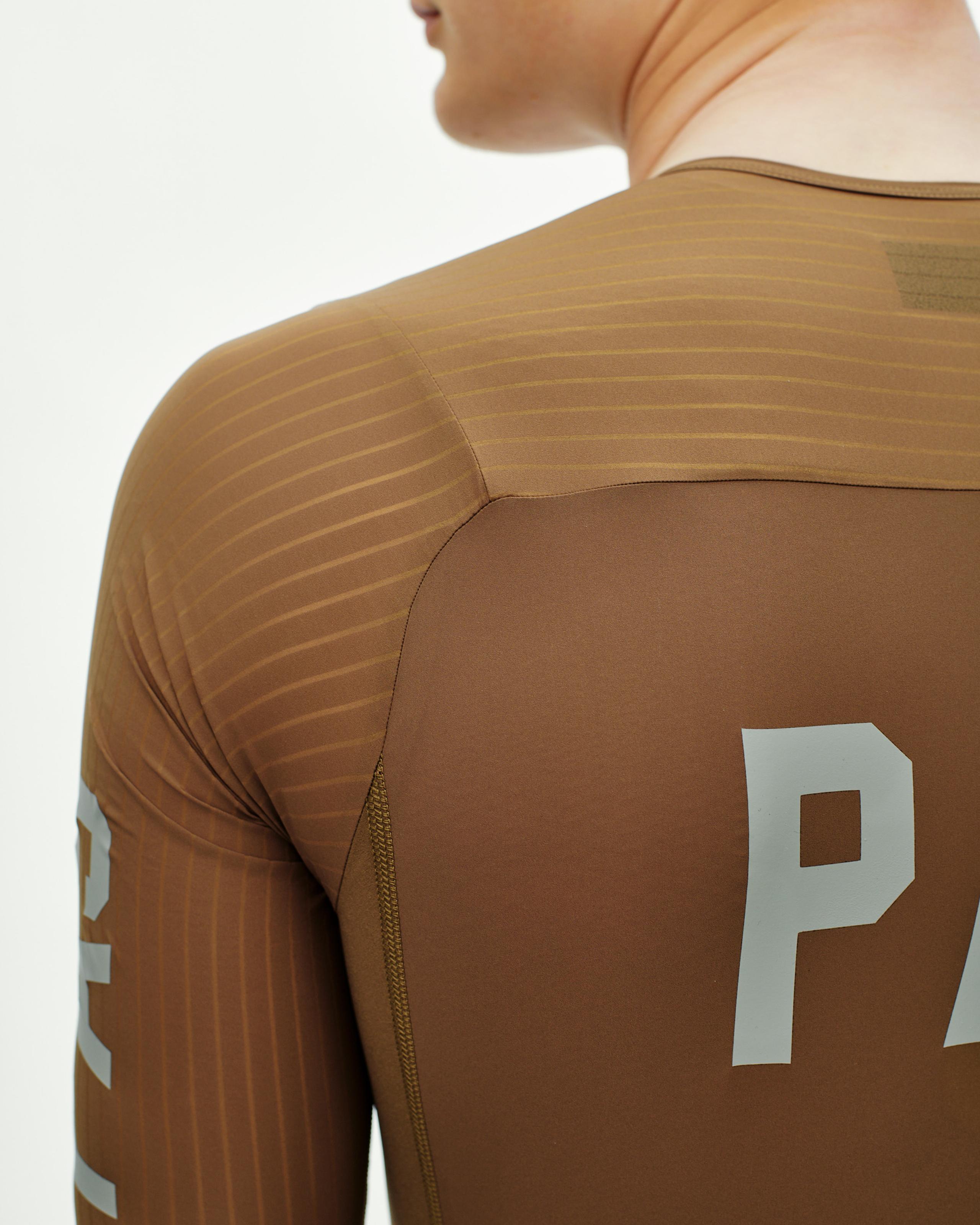 Brown PAS Mechanism Pro speedsuit on model, rear three-quarter view with ribbed shoulder panels