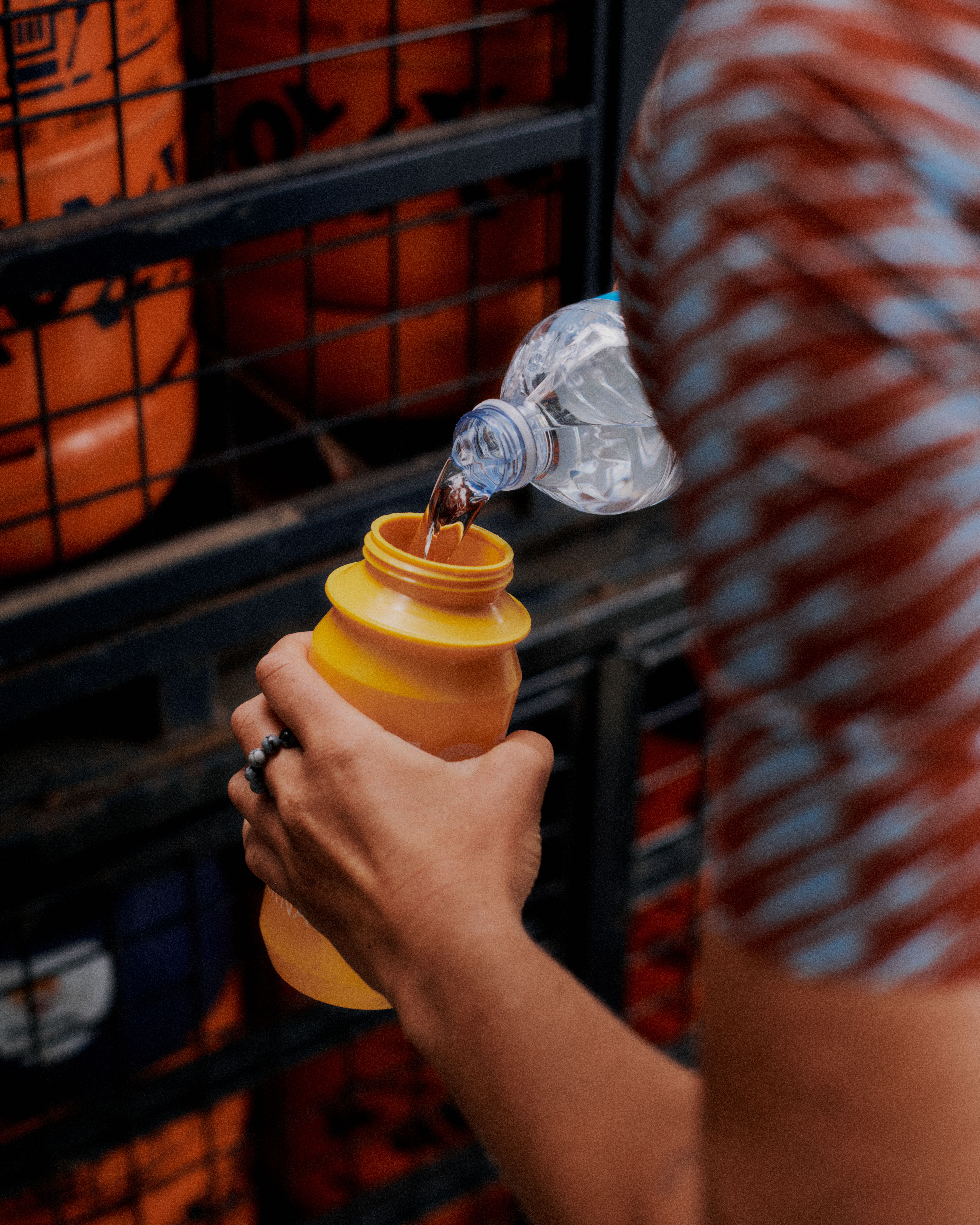 Cyclist pouring water from bottle into yellow collapsible cup during urban ride