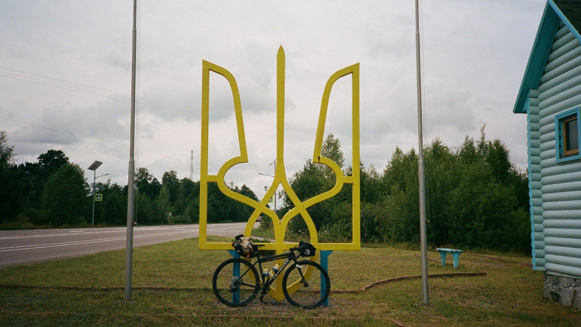 Bicycle parked in front of large yellow Ukrainian trident monument along rural roadside