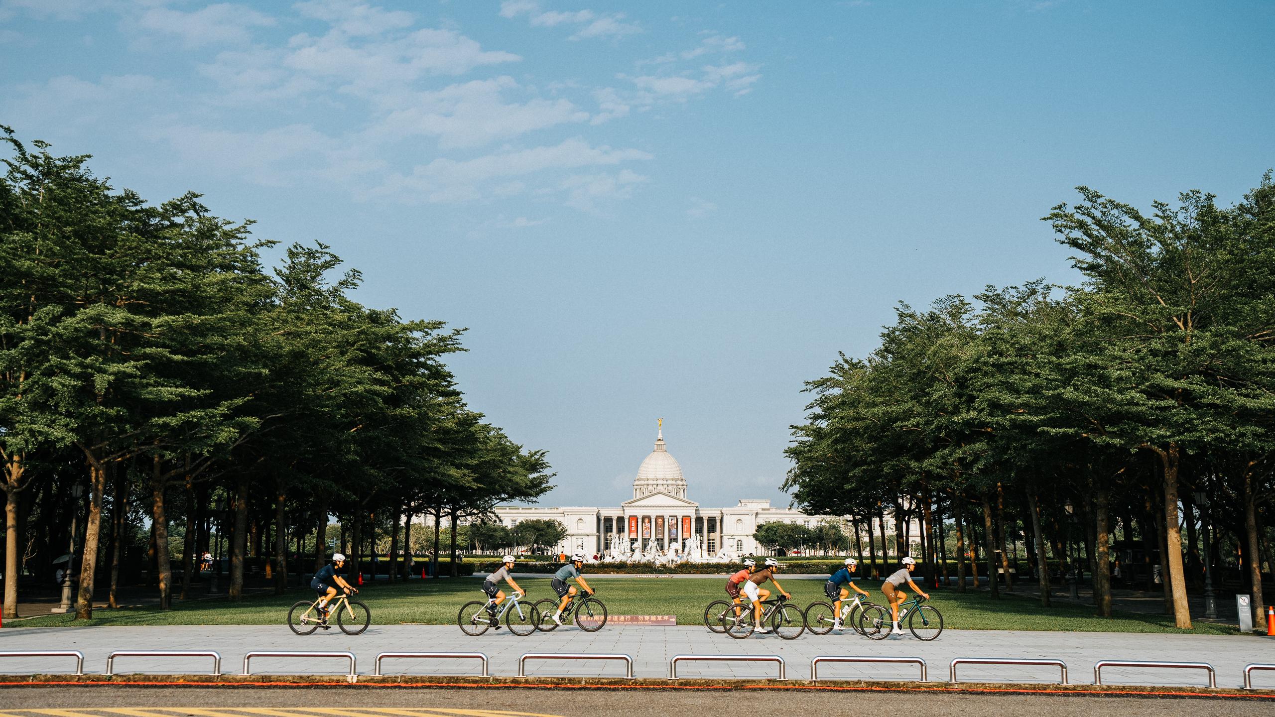 Group of cyclists riding past government building with dome and columns