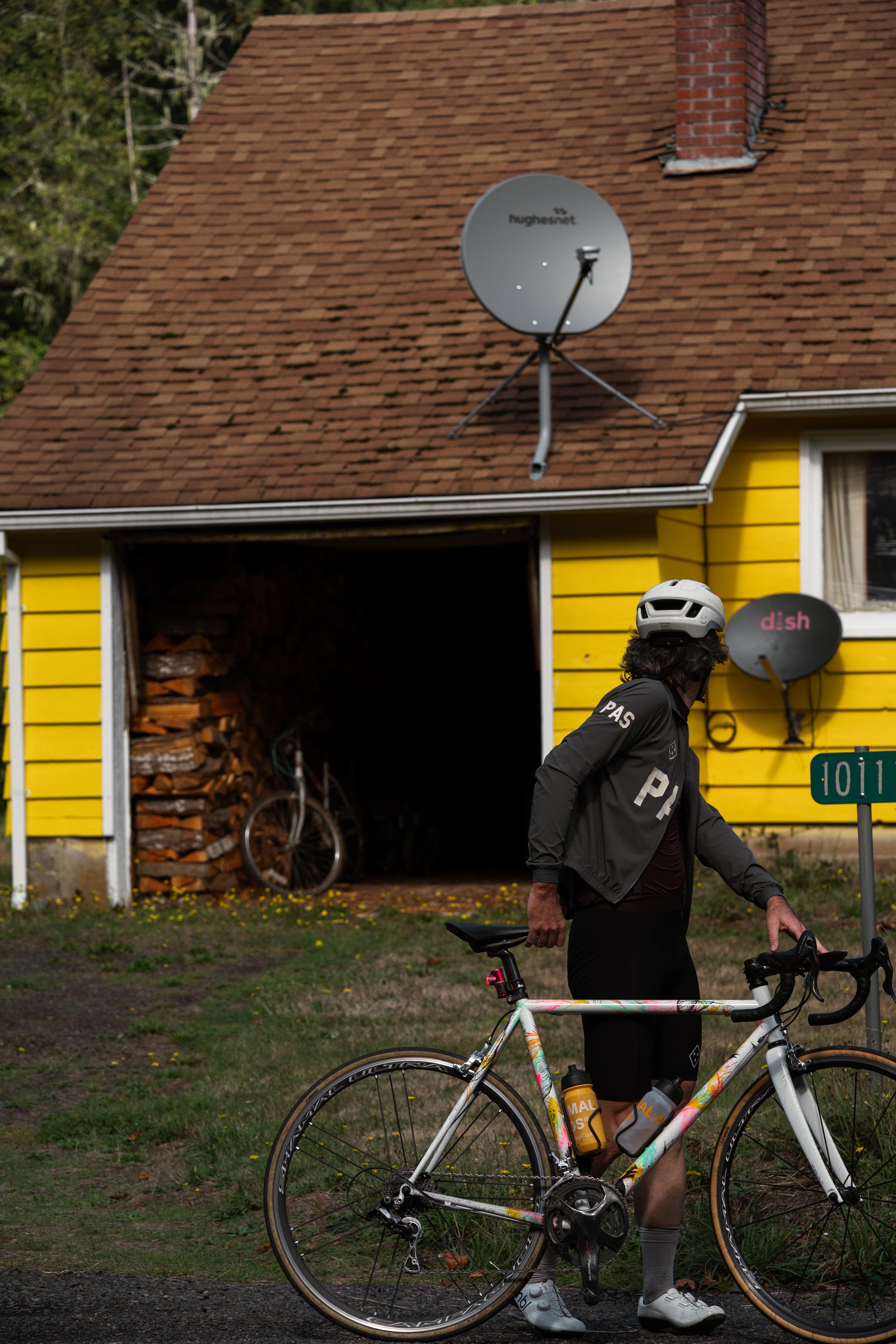 Model wearing dark grey long sleeve jersey with back lettering, standing with colorful road bike