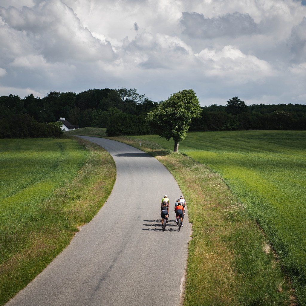Two cyclists riding on winding country road through green fields and rolling hills