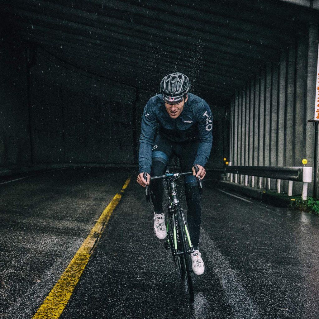 Model wearing dark blue cycling kit on time trial bike in rainy tunnel