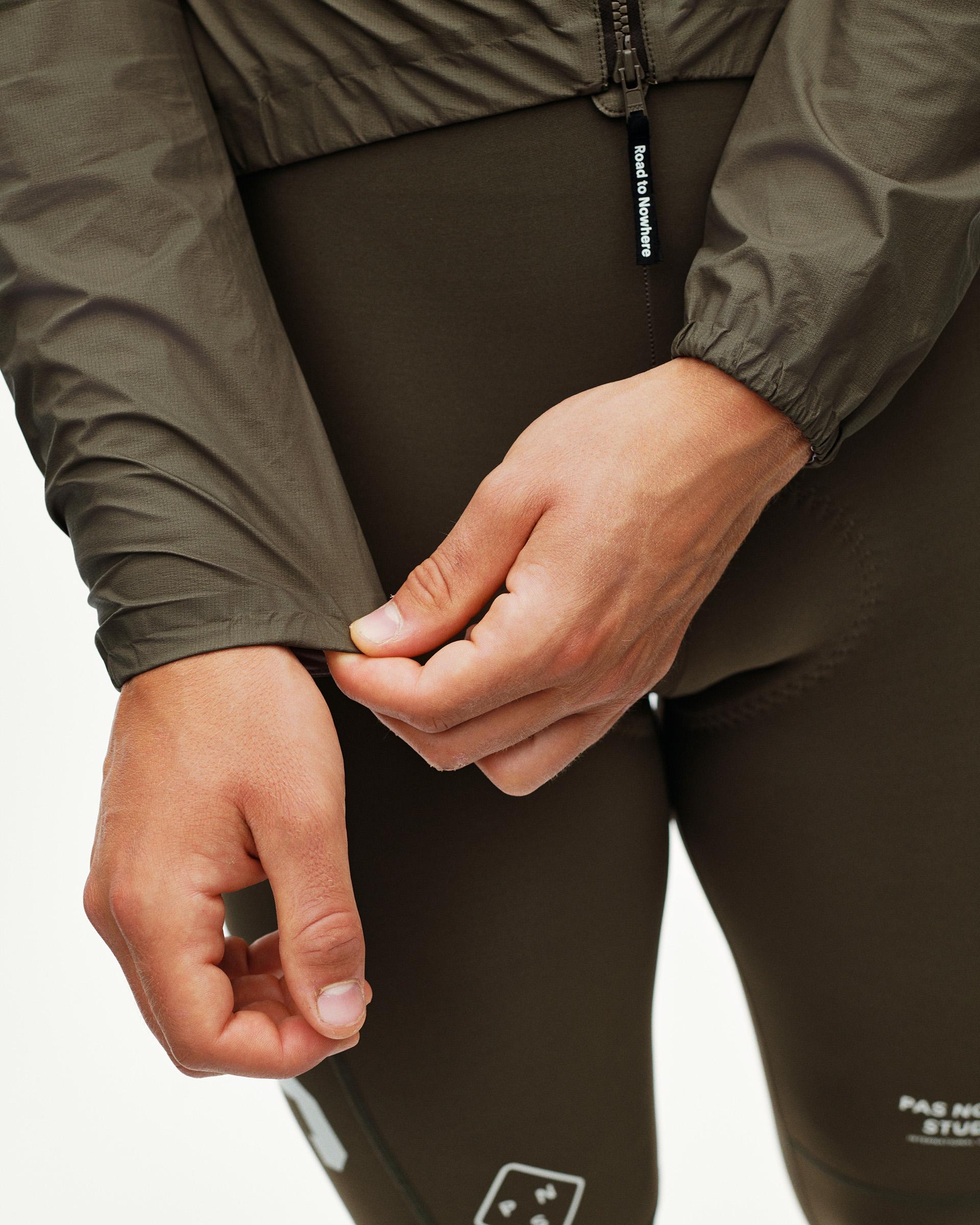 Dark Earth khaki PAS Mechanism cycling rain jacket, detail on model showing elasticated cuff and branded zip puller