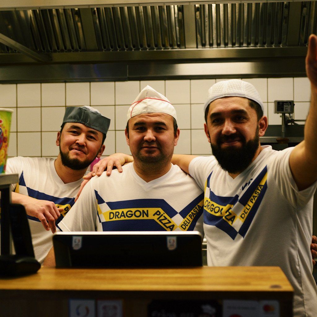 Three chefs wearing white cycling jerseys with blue and yellow stripes in restaurant kitchen