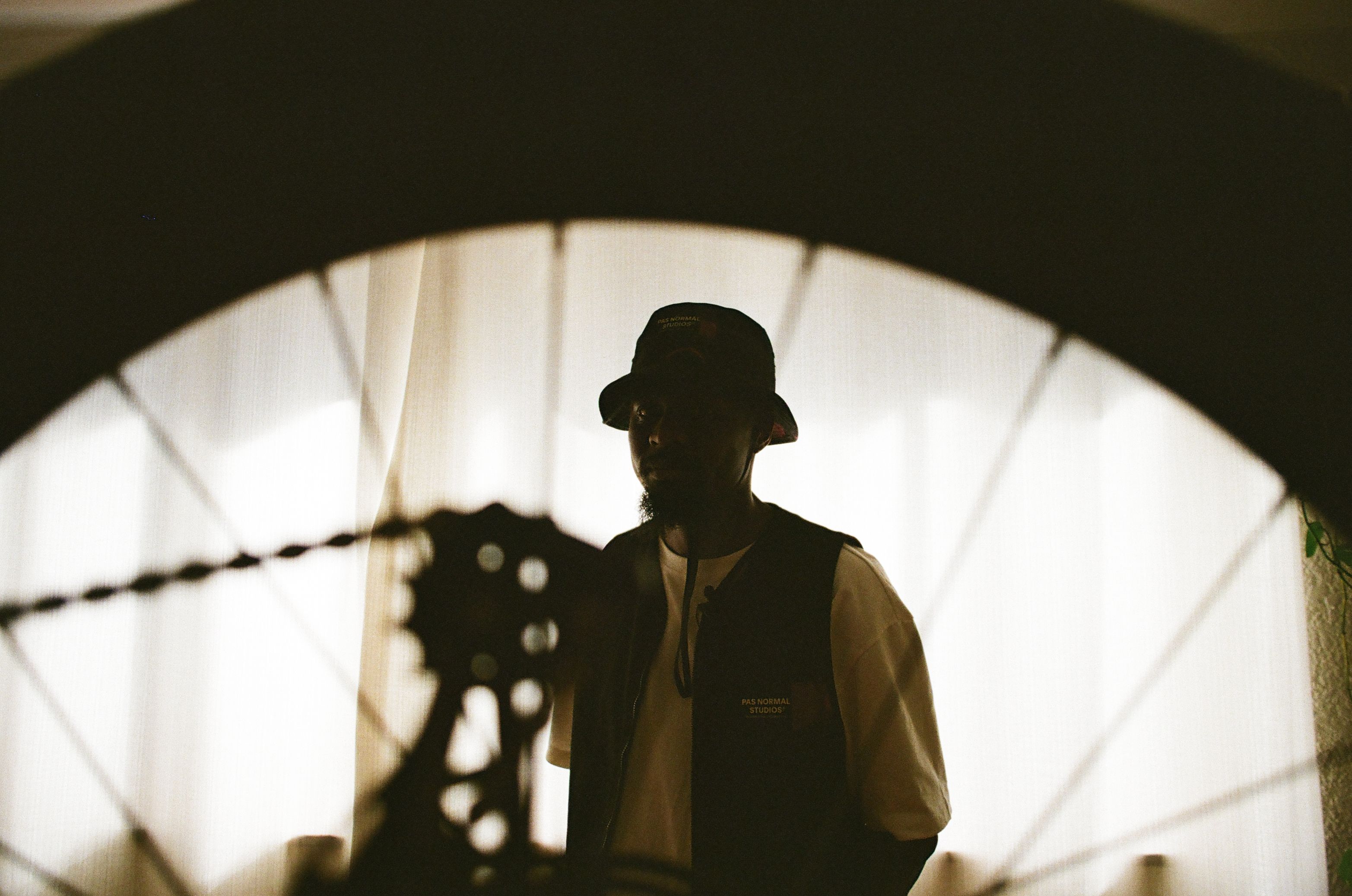 Model wearing dark bucket hat and vest under concrete archway