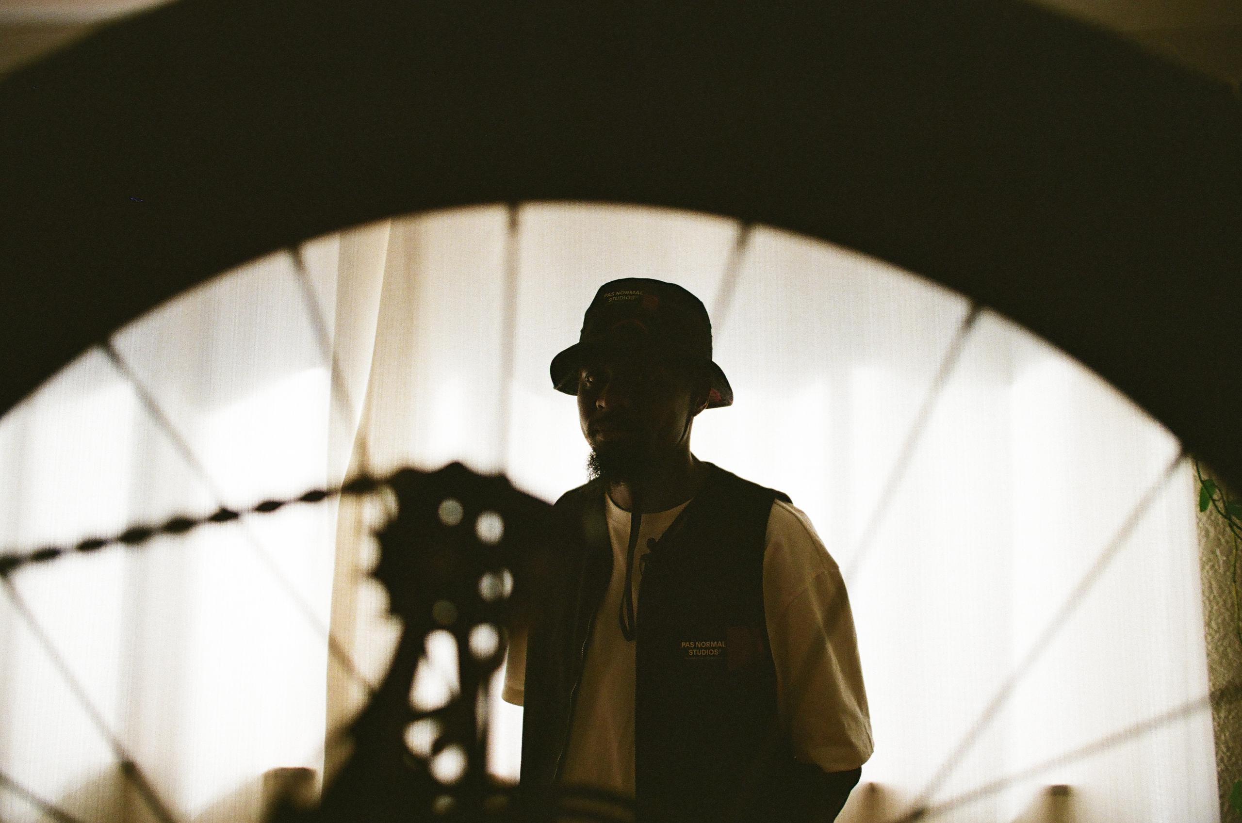Model wearing dark bucket hat and vest under concrete archway