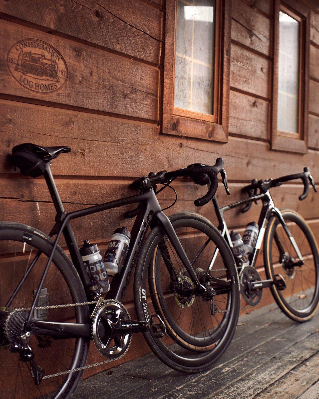 Two road bikes parked against rustic wooden cabin wall with windows