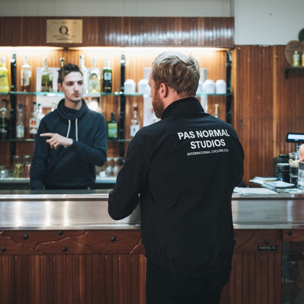 Model wearing black jacket with white back lettering in cafe setting