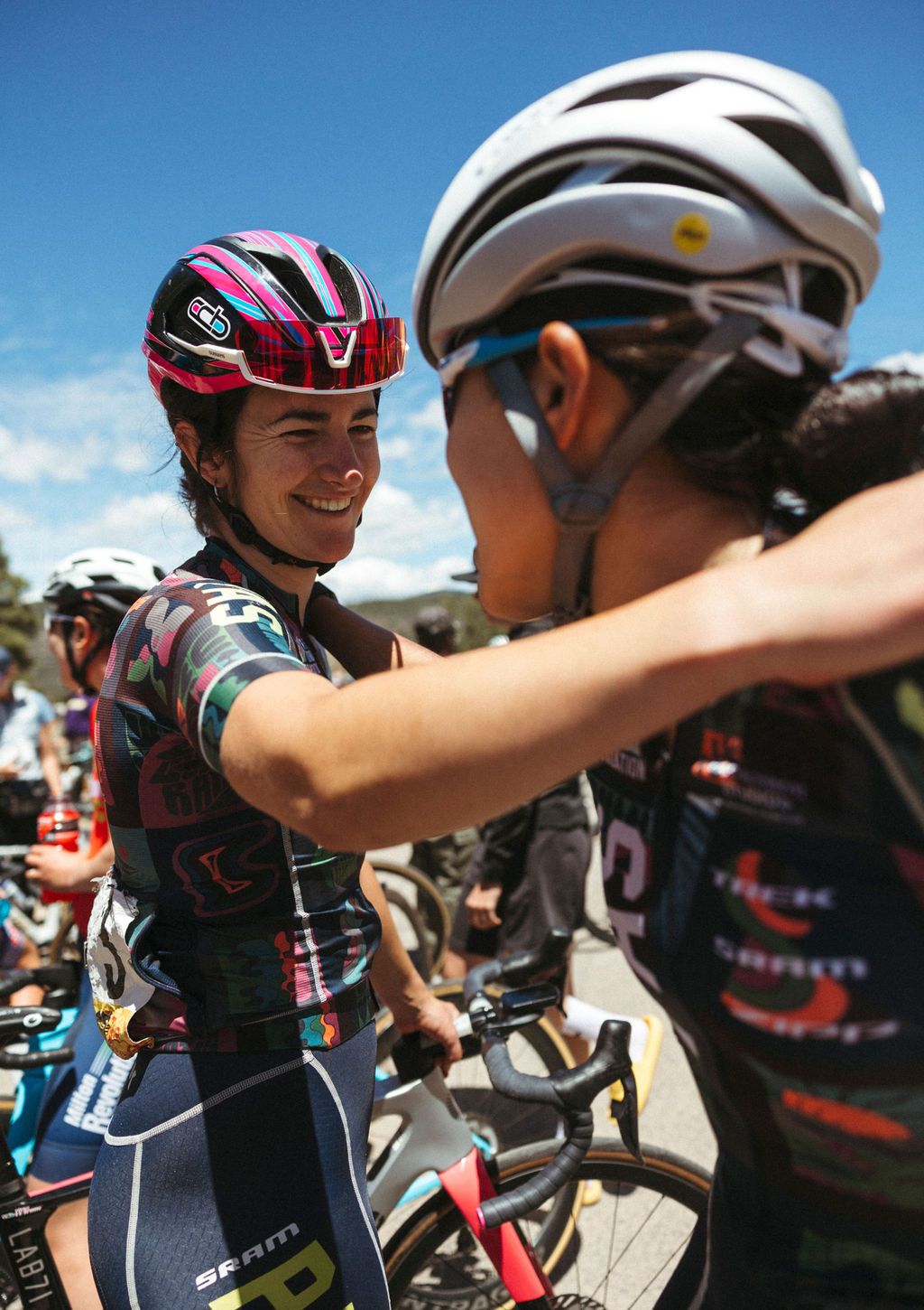 Female cyclist in multicolored patterned jersey embracing teammate at cycling event