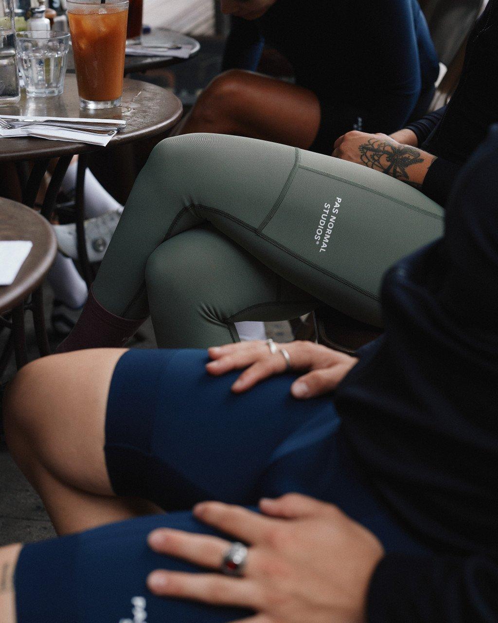 Model wearing olive green cycling shorts with logo at cafe table