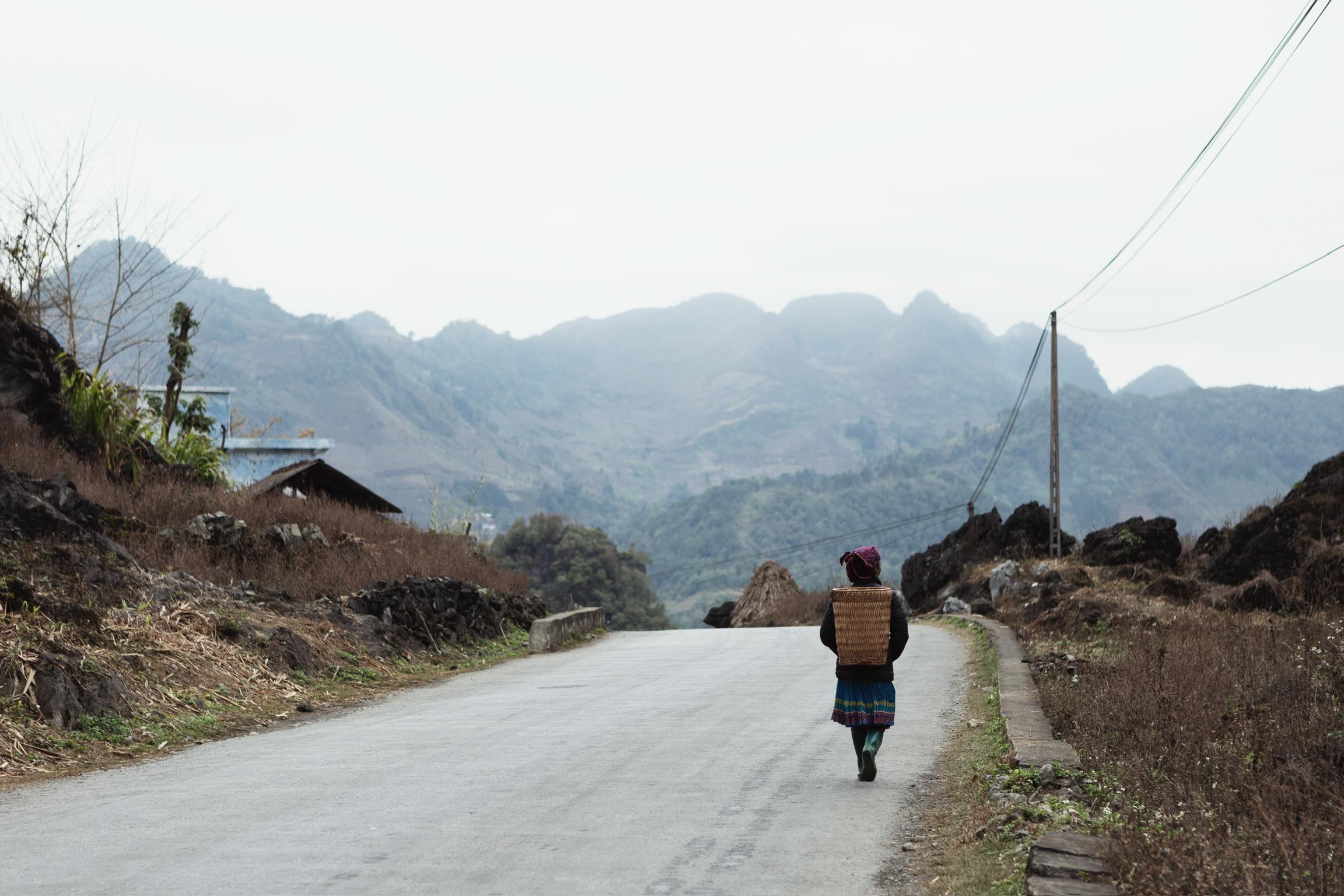 Person walking on mountain road carrying basket with dramatic valley landscape in background