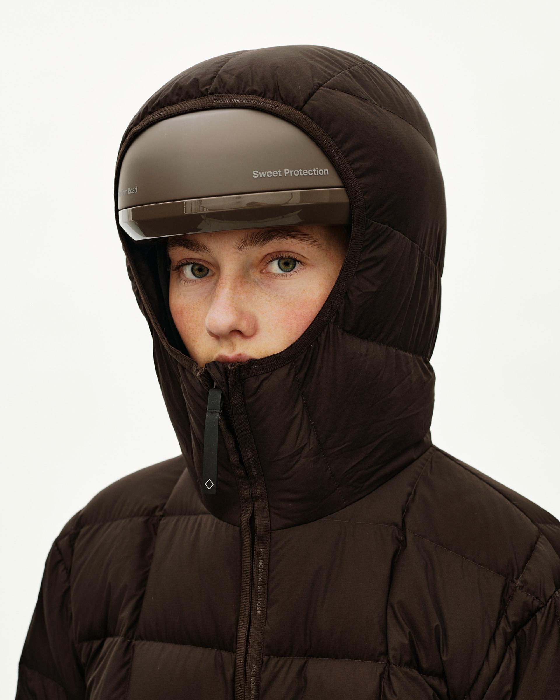 Dark Coffee brown Off-Race Down Liner jacket on model, front view with quilted hood up and Sweet Protection helmet