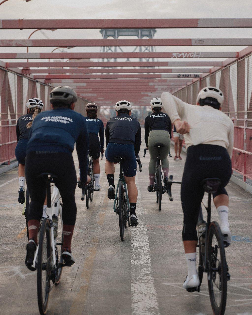 Group of cyclists riding through bridge tunnel wearing navy jerseys with logo branding
