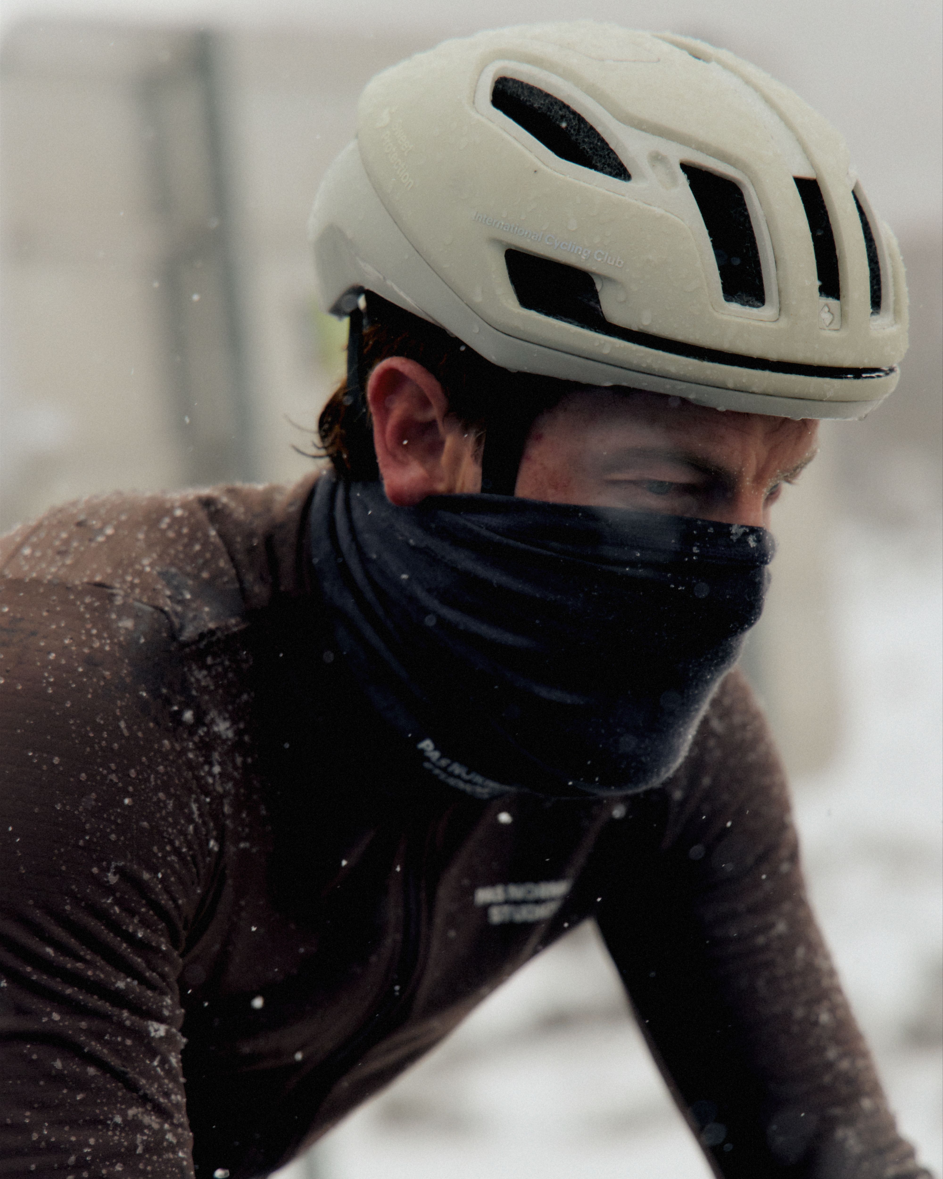 Model wearing off-white cycling helmet and black face covering in snowy conditions