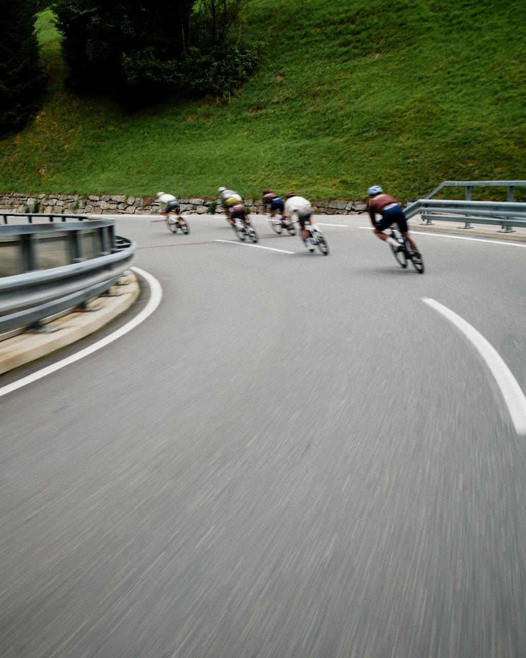 Group of cyclists in aerodynamic position racing on mountain road curve with motion blur